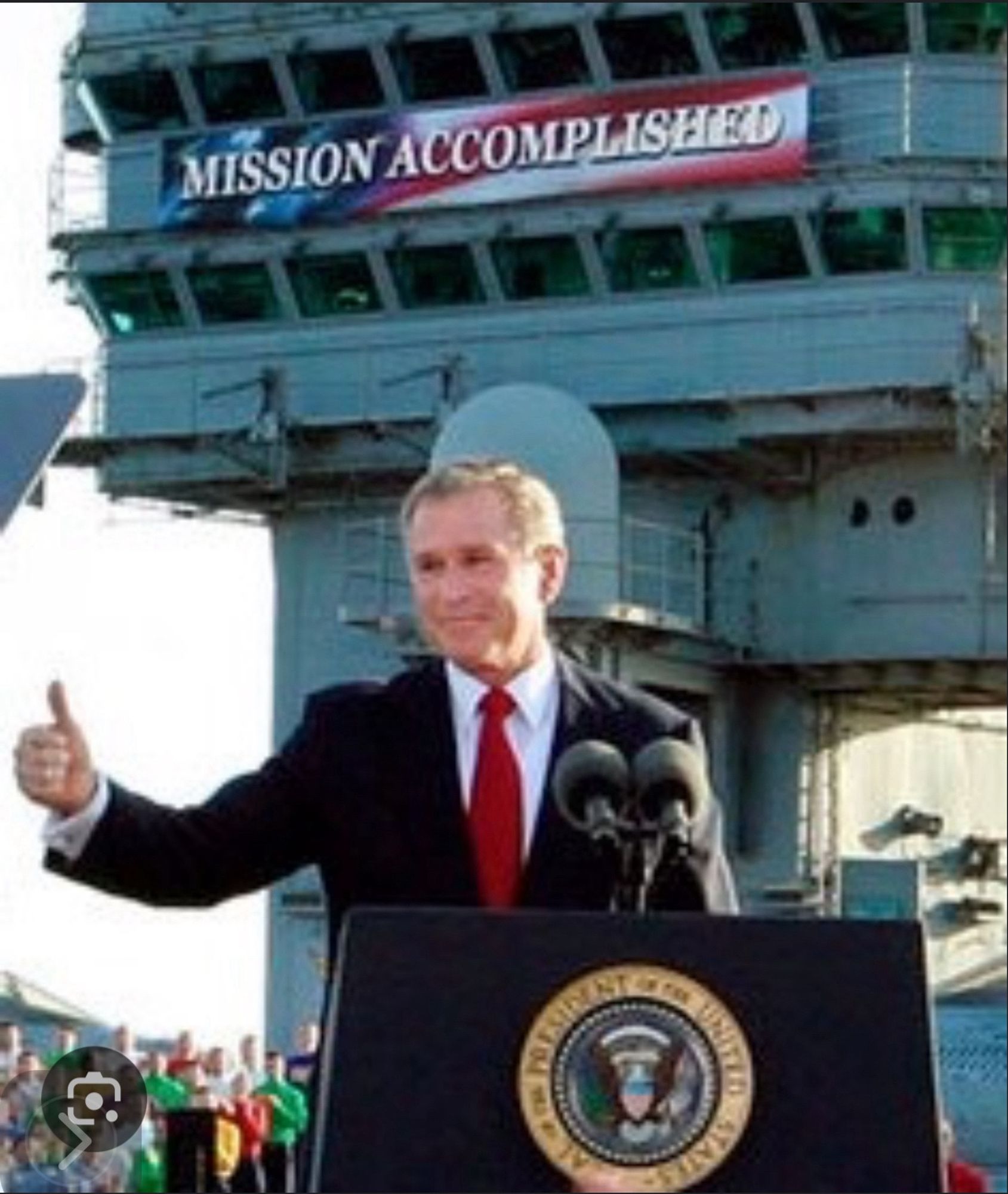 George W Bush on a war ship  giving a thumbs up under a banner “Mission Accomplished”