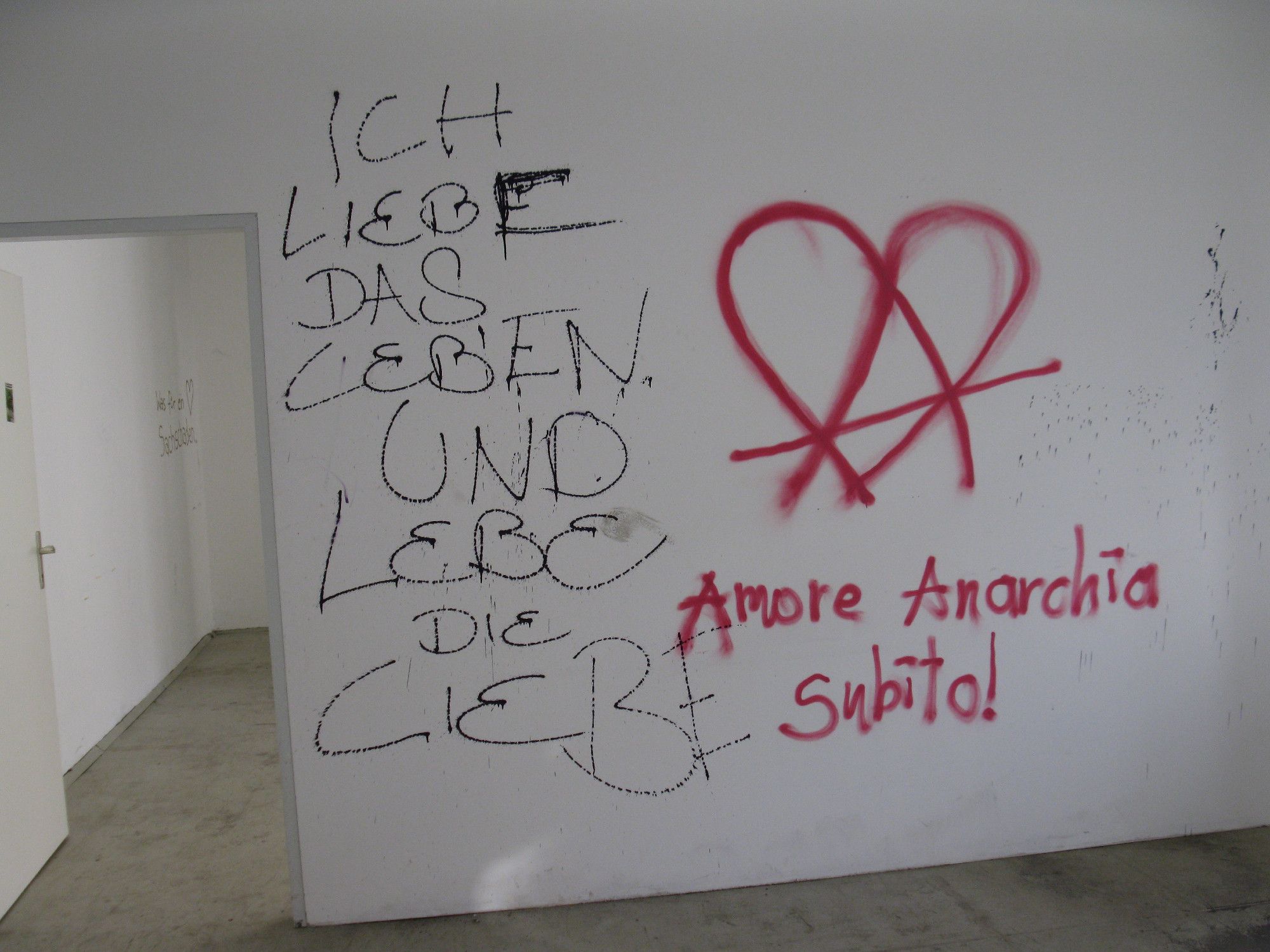 An eine Wand hat jemand geschrieben: "Ich liebe das Leben und lebe die Liebe". Daneben ein Herz und Anarchie-A mit der Schrift: "Amore Anarchia subito!"