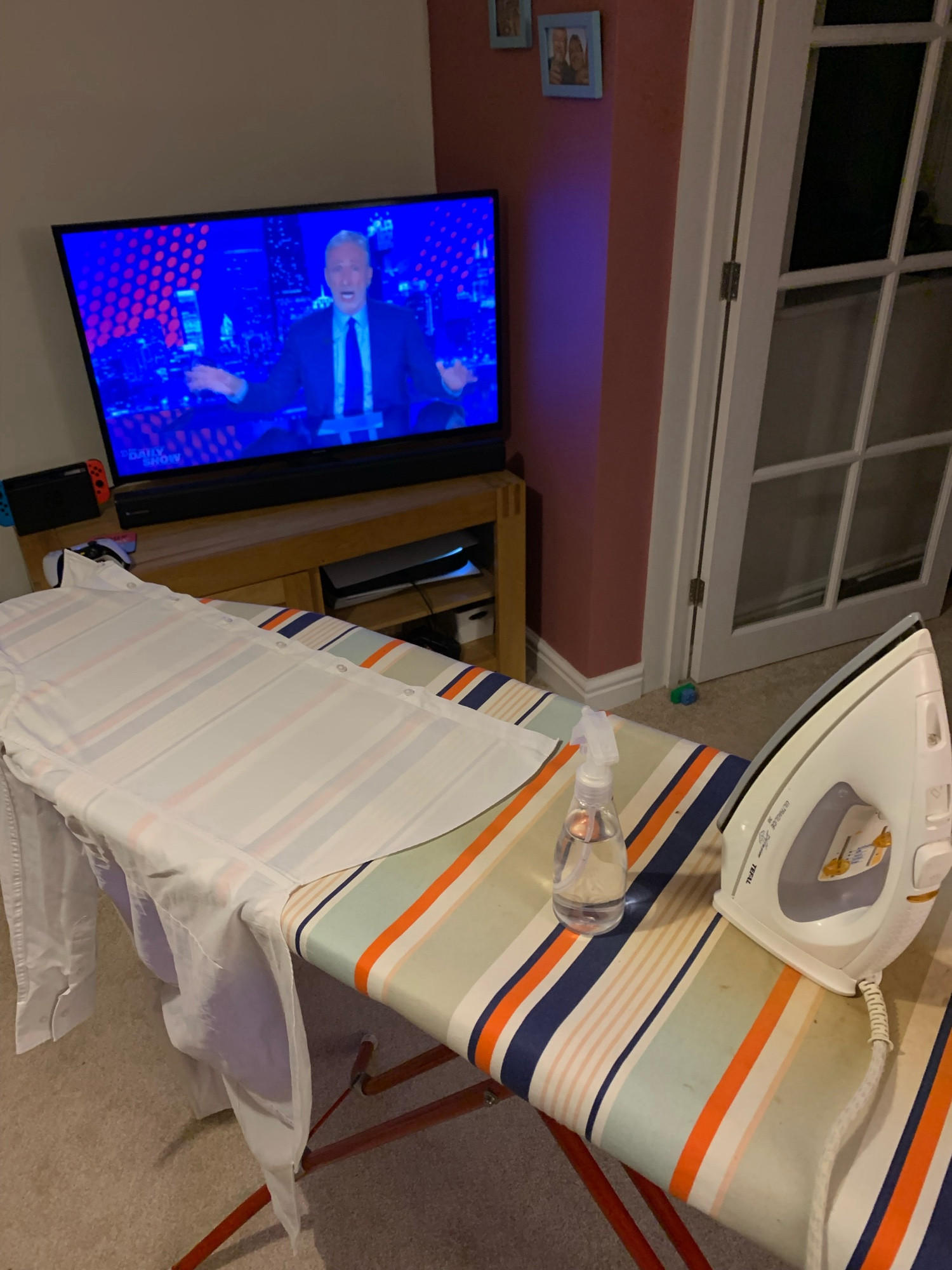 Photo of an ironing board with an iron, spray bottle, and white shirt on it.