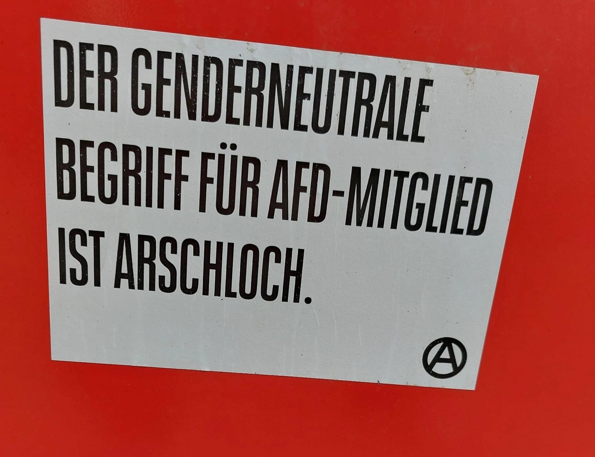 Weißer Kleber auf rotem Grund mit schwarzer Schrift in Versalien.
Aufschrift: "Der genderneutrale Begriff für AfD-Mitglied ist Arschloch"