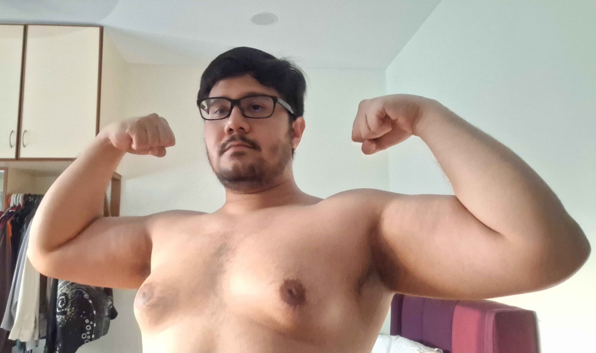 A picture of me shirtless, both my arms are raised, and I am flexing both of them. I am fat yet muscular.The sun is shining from the left, gently covering me with a golden light.