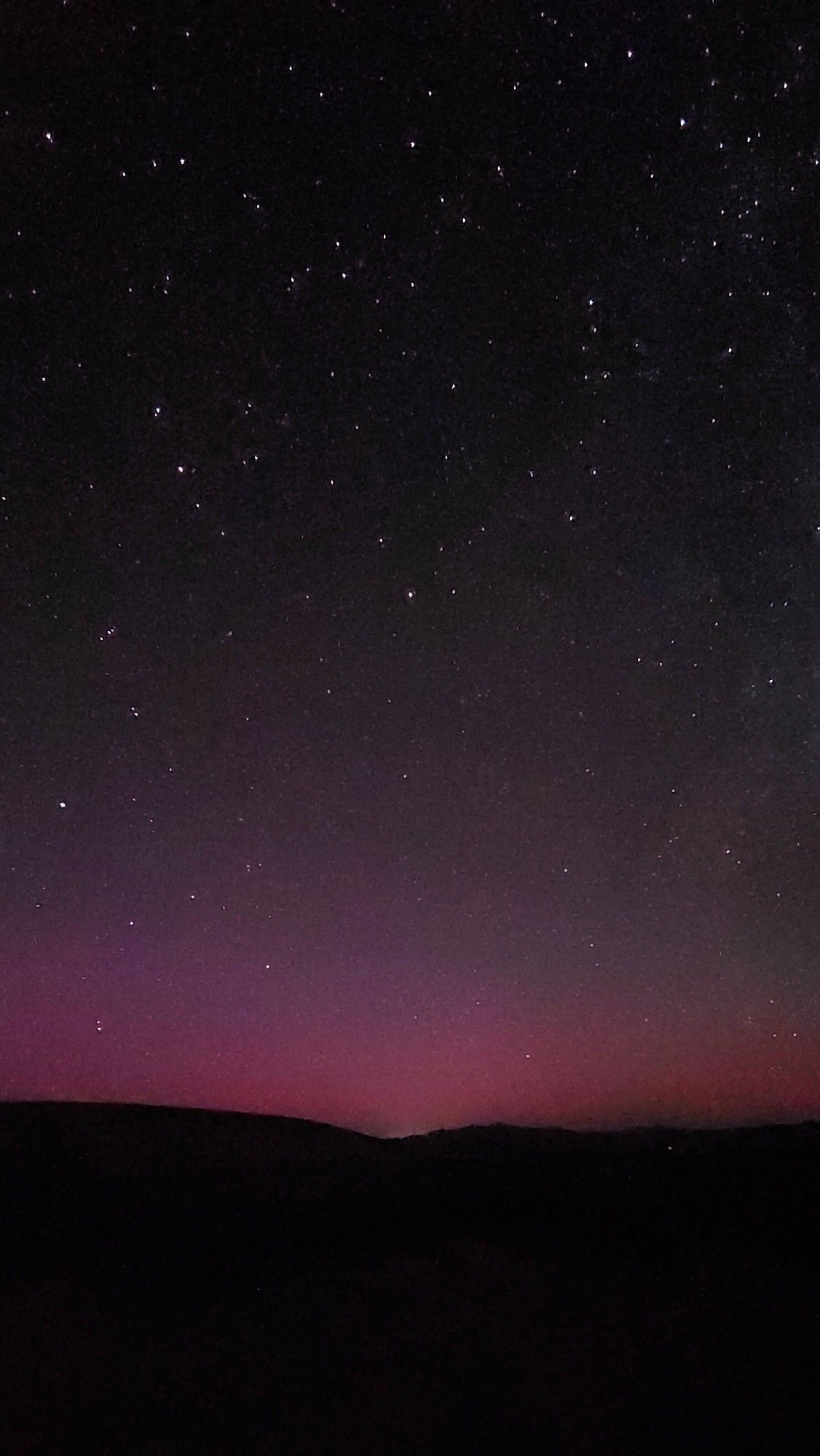 A serene night sky featuring a gradient of deep purple to black, dotted with numerous stars over a shadowy landscape.