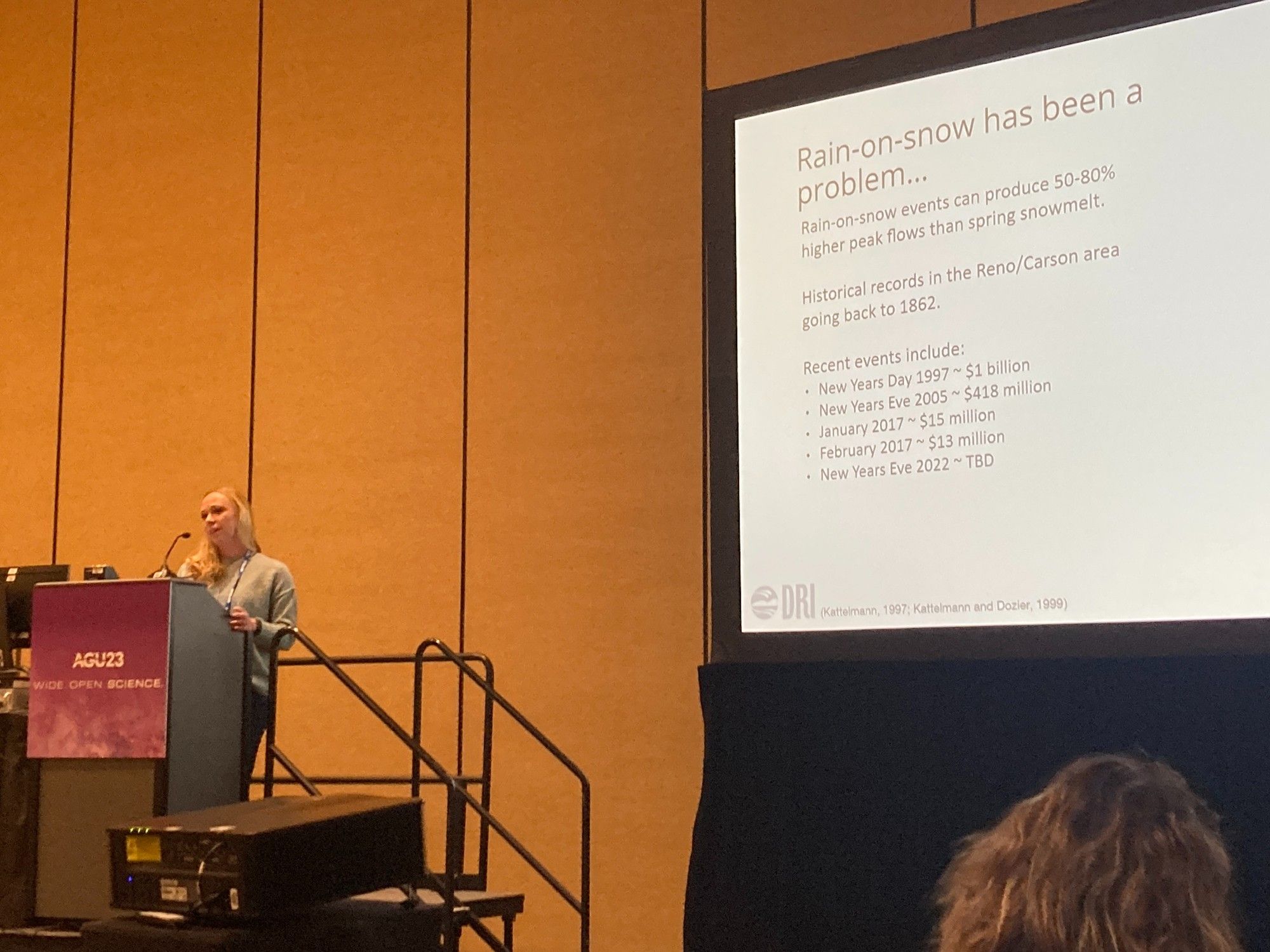 Anne Heggli presenting at the podium at AGU23 with her presentation up on the screen behind her.