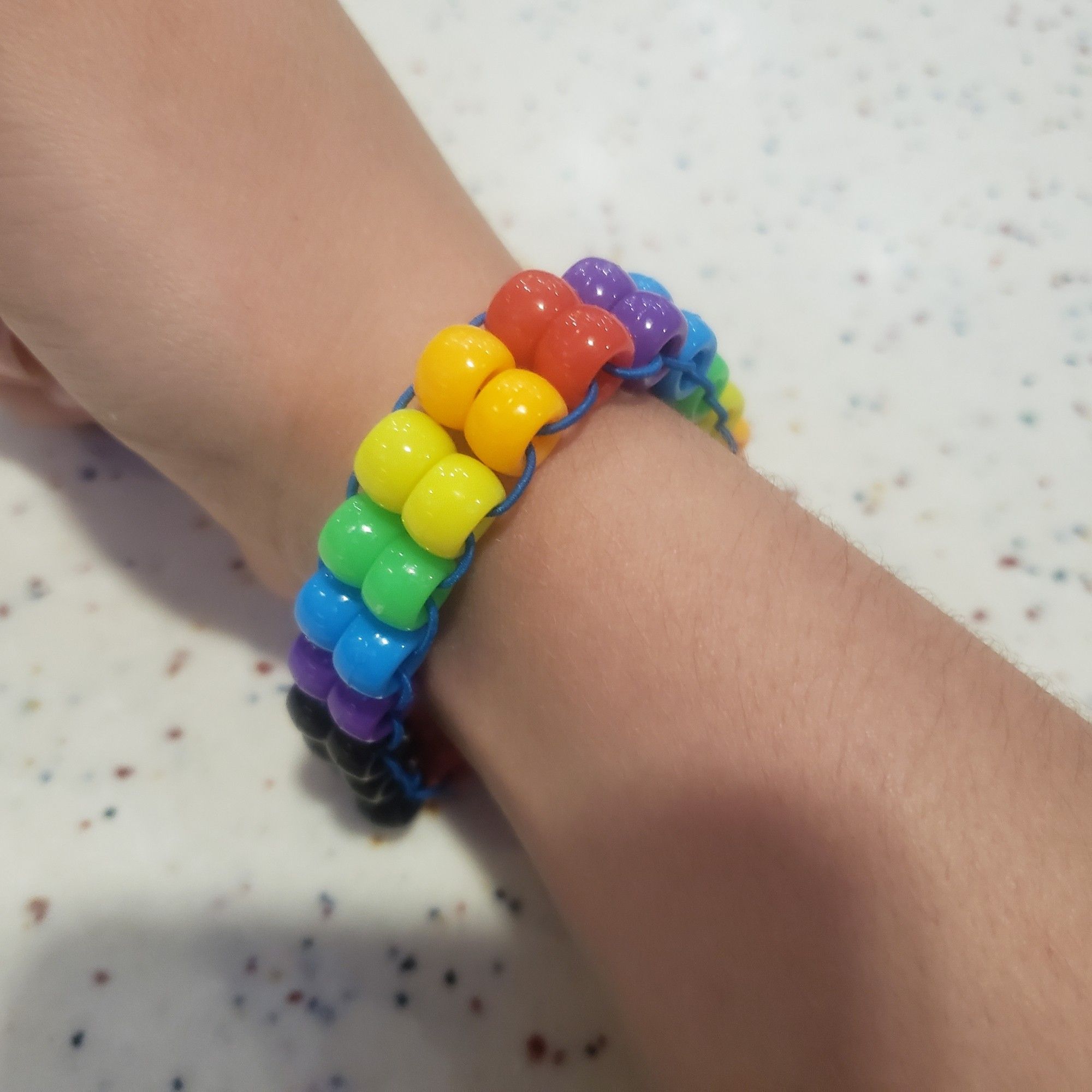 A rainbow + black, 2-bead-wide kandi bracelet w blue string