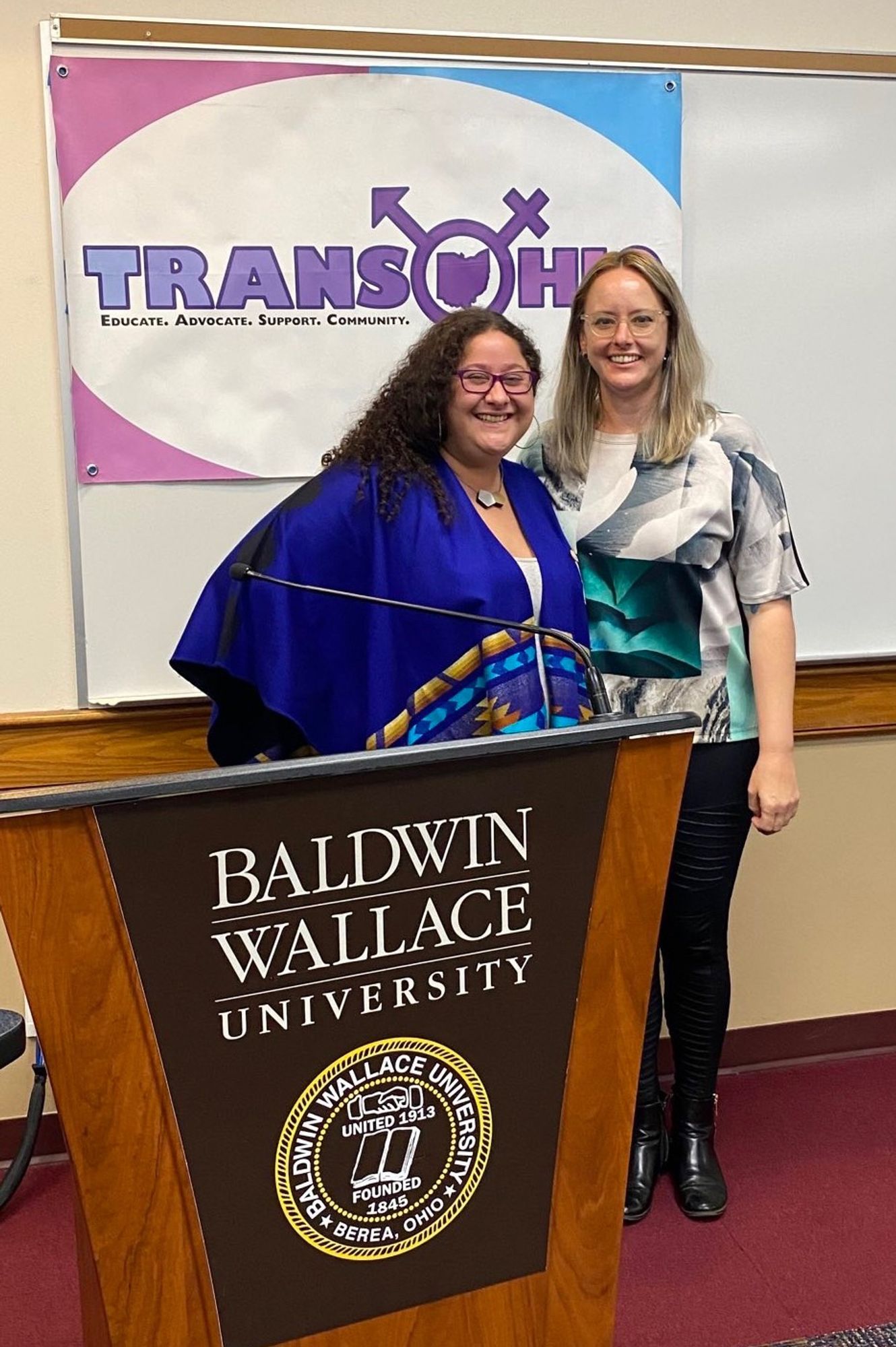 OP stands next to co-presenter in front of a TransOhio banner and behind a Baldwin Wallace University lecturn