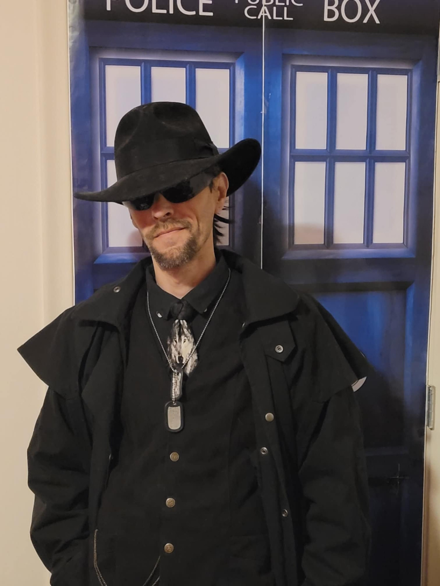 Me in front of a TARDIS door (my closet) for character reference for my Chronicles of the Lone Wolf novel series. Black, Australian-cut fedora, black sunglasses, black button down and vest with pocketwatch, wolf necktie, dogtags, and black oilskin duster.