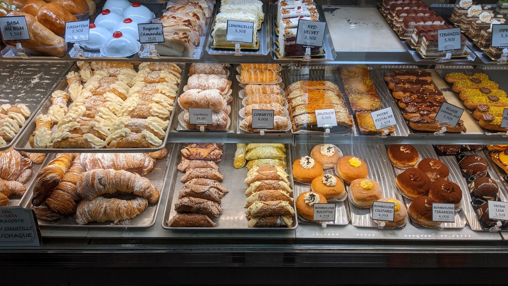 A shelf full of Italian pastries including different kinds of cannoli, bomboloni, and cakes.