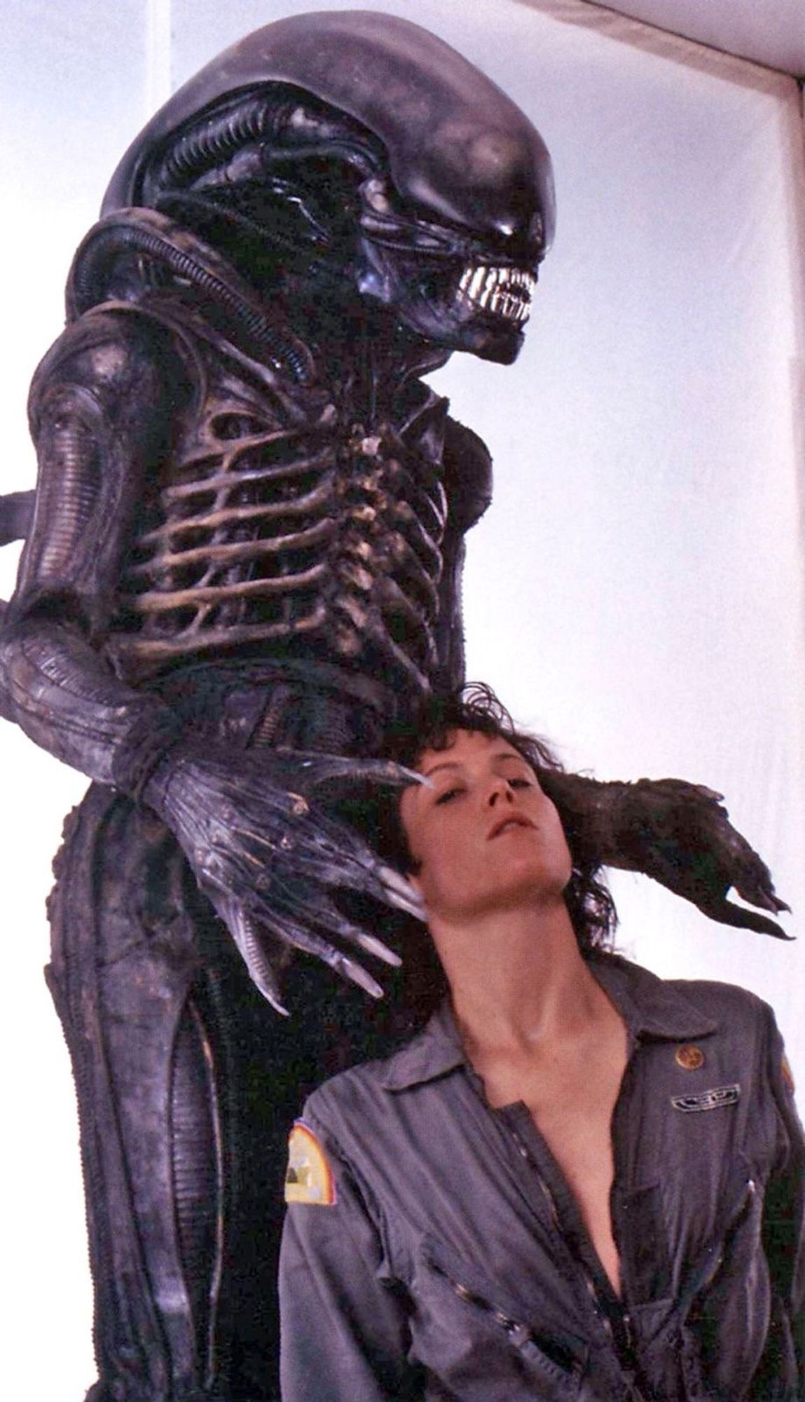 A xenomorph alien with its hands about to clutch Sigourney Weaver in a low cut flight suit looking seductive