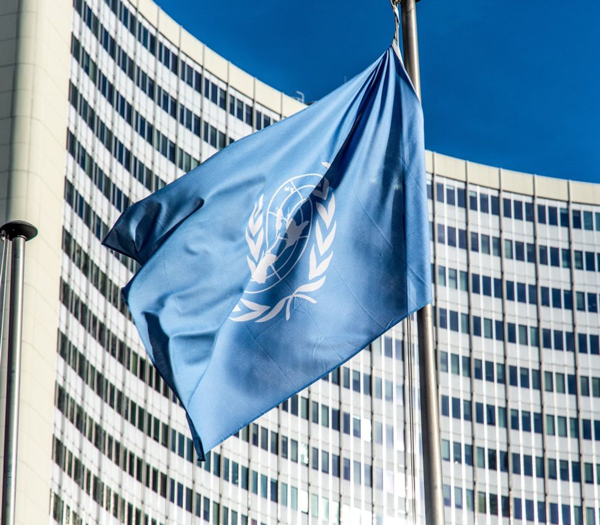 Das Bild zeigt die blaue UN-Flagge vor UN-Gebäude und blauem Himmel