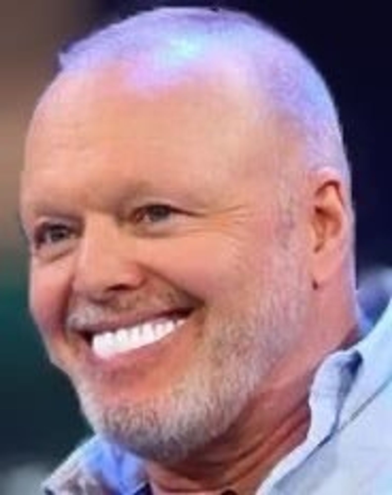 A smiling man with a short, light-colored beard and short hair, wearing a blue shirt. The background appears blurred.