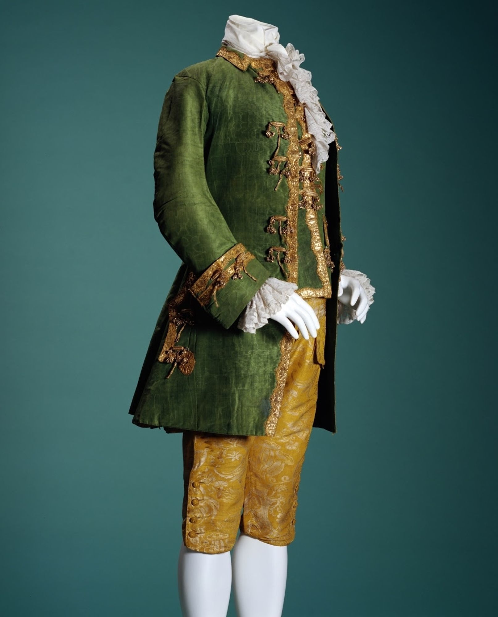 a mannequin wearing a men's outfit from the 18th century. it has a green jacket with gold trimmings, a similar waistcoat and gold breeches.