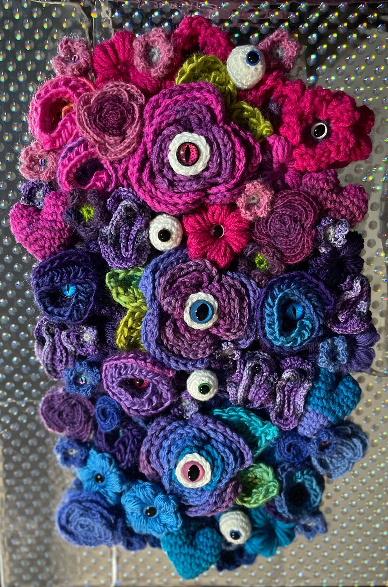 Crochet collage of flowers, eyeballs and hearts, in blues purples and pinks.