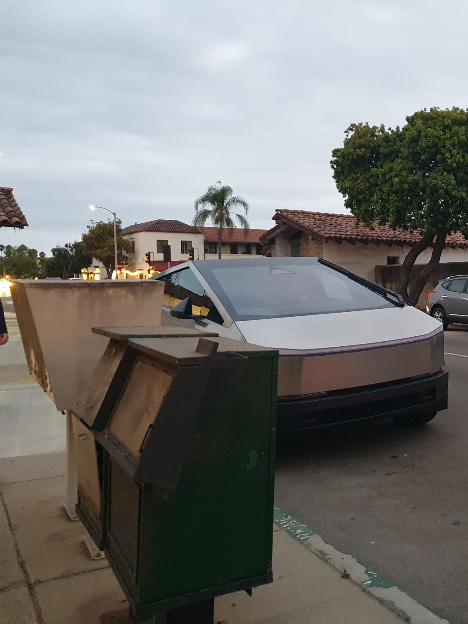 A cybertruck parked near metal boxes that look vaguely like letterboxes, and that have similar angles as the cybertruck