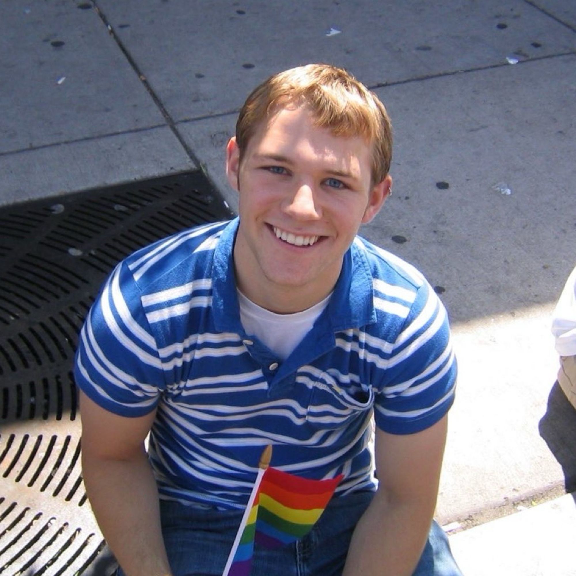 It’s me again! I’m sitting on the ground at the Chicago Pride Parade in 2004. I’ve still got the spark of youth in my eyes, a longer haircut, blue and white striped polo from Hollister, and jeans. I’ve also got a little Pride flag in my hand. It was a good day.