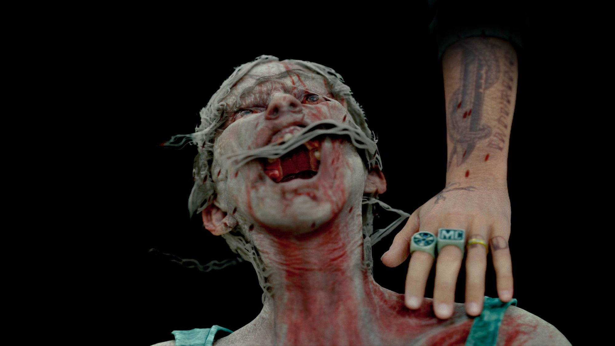 A woman zombie from the shoulders up. She is tilting her head back with her mouth wide open and screaming. Her hair is blowing across her face. The left hand and forearm of Deacon (the protagonist from Days Gone) emerge from a black background. He is placing his hand on the zombies left shoulder. 