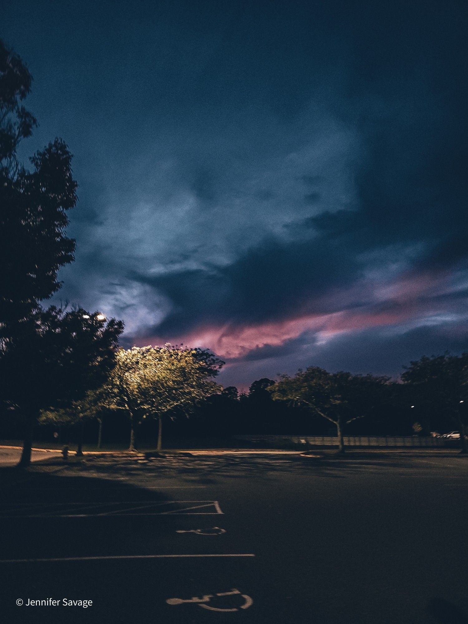 A faded photograph of trees and handicapped parking in a parking lot with a pink and blue sunset highlighting the clouds in the distance.