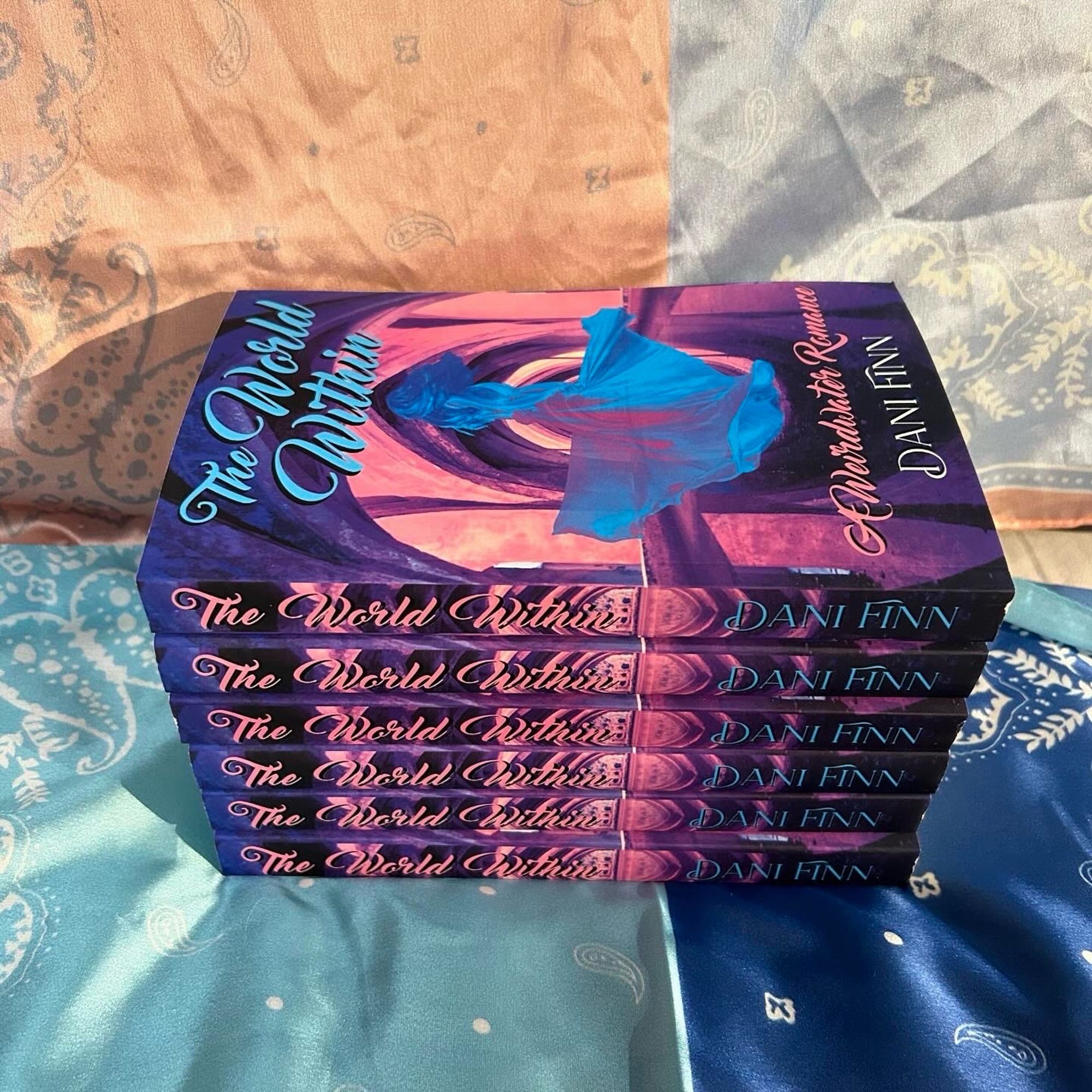 6 Copies of The World Within, spine out. The World Within (swirly light blue font near the top), A Weirdwater Romance (swirly pink font beneath the main image) by Dani Finn (plain but slightly swirly white font near the bottom). The background image is of an arched temple pool in pink, lavender, and blue/purple tones. Floating in the center, slightly transparent, is a light blue and pinkish purple woman in a twirling dress, almost otherworldly.