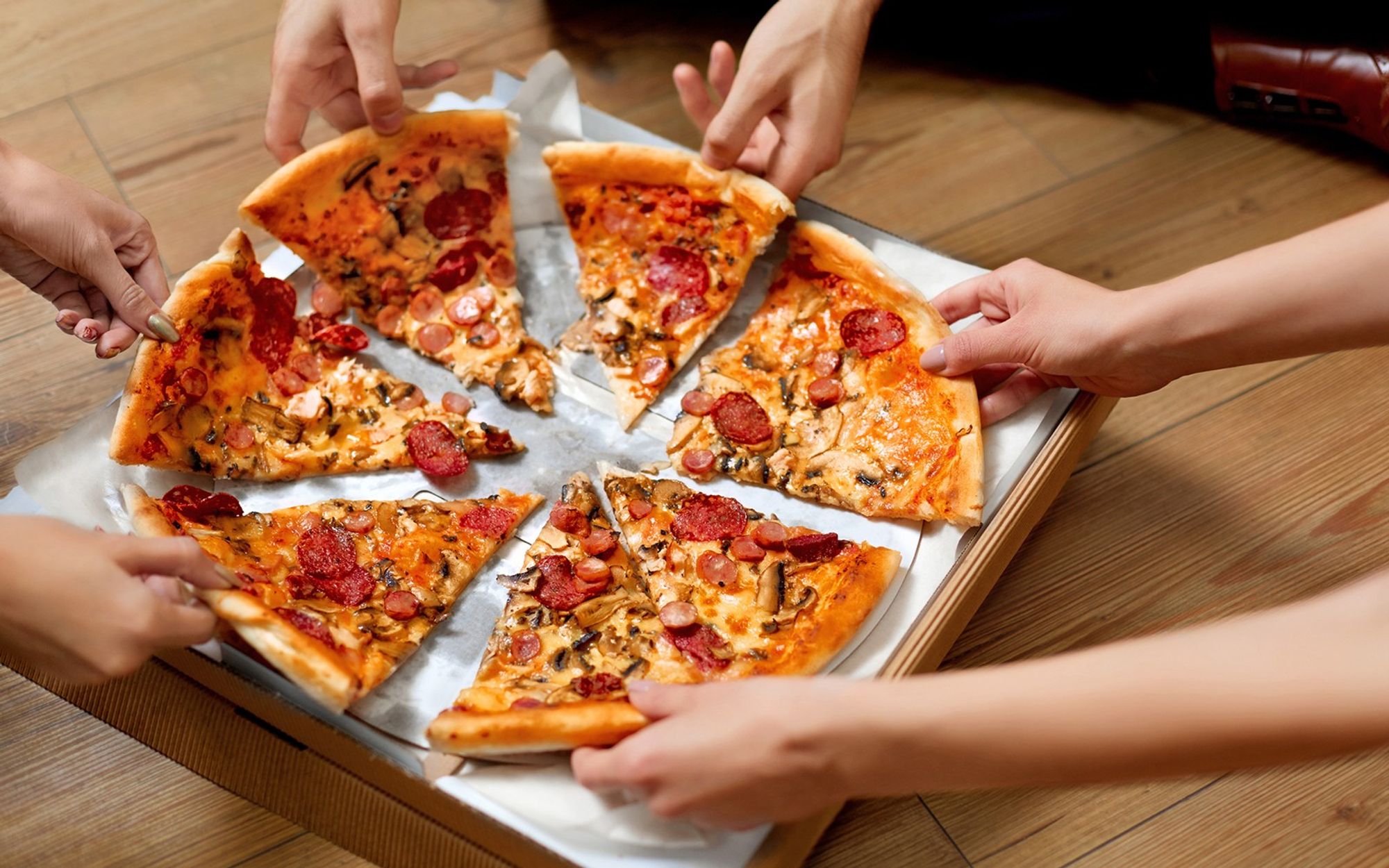 People's hands taking pieces of pizza