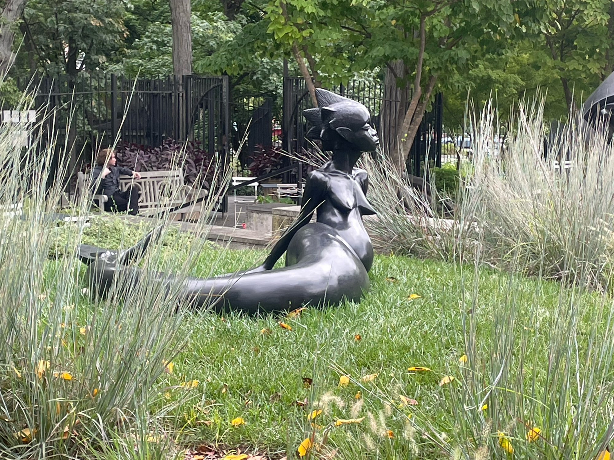 Sculpture of mermaid-type figure in grassy area, with a determined, complex emotion on her face.