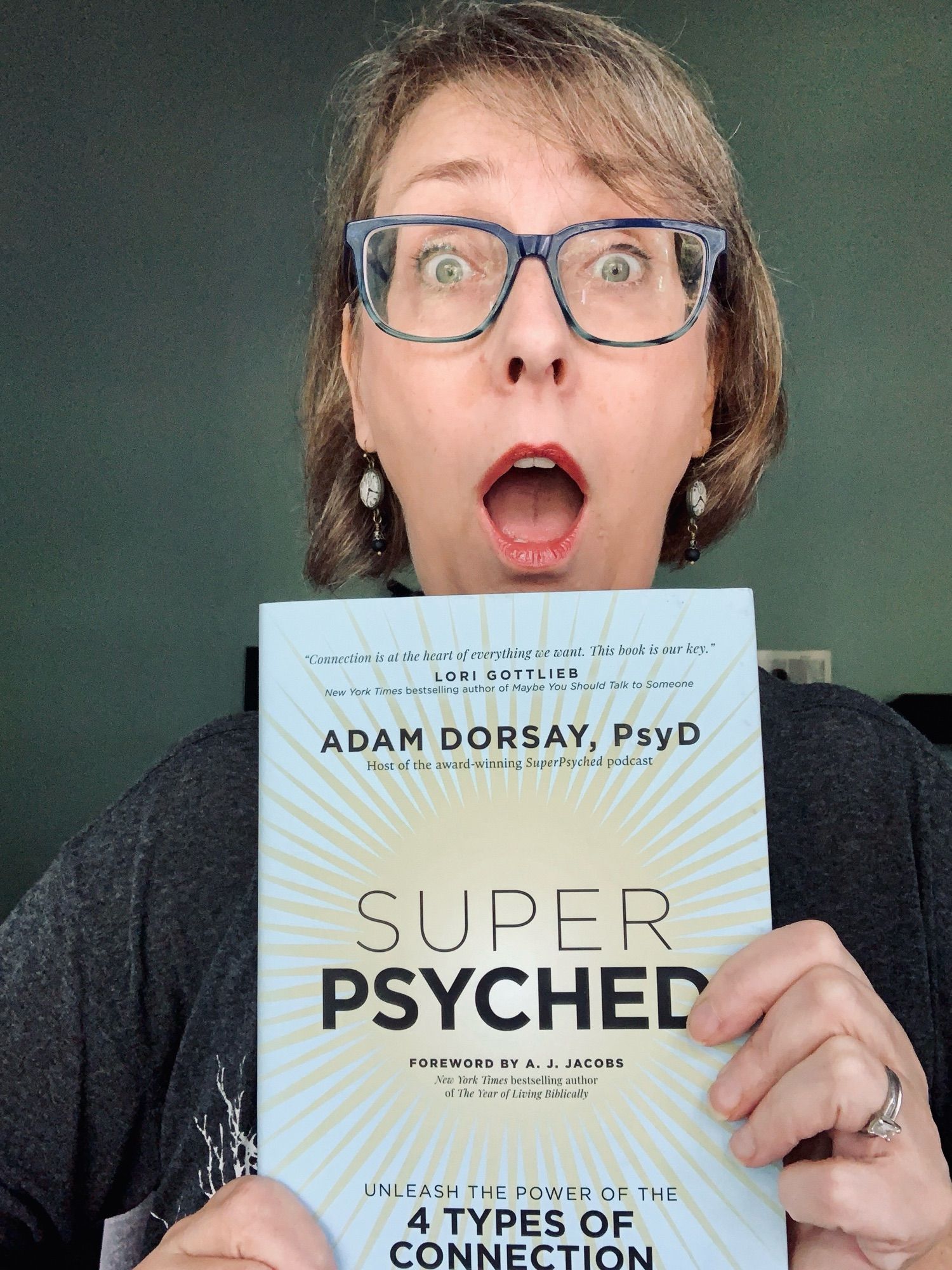 A white woman with a surprised expression holds a book titled SUPER PSYCHED: Unleash the Power of the 4 Types of Connection.