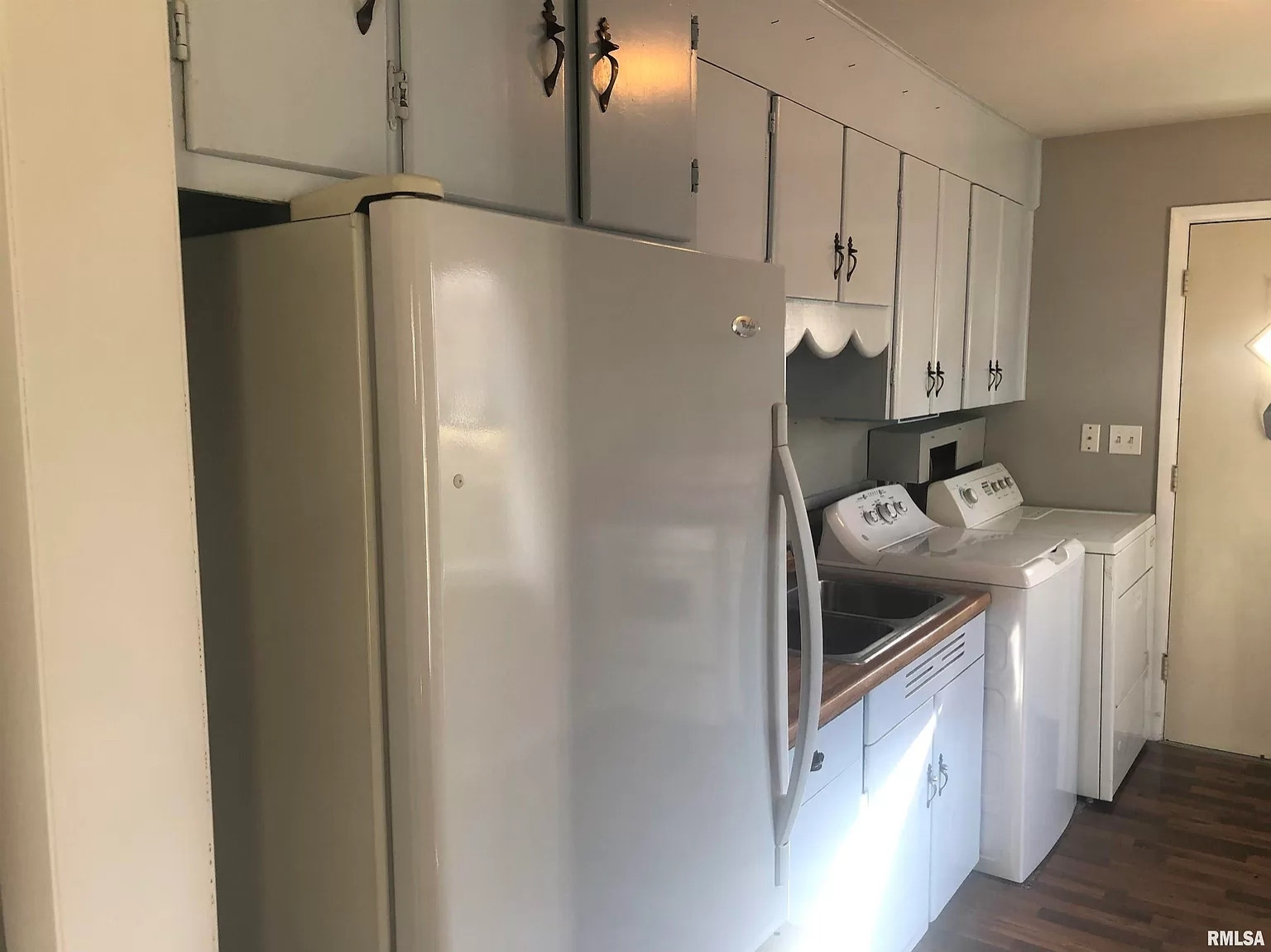 a kitchen wall with a refrigerator next to a small segment of counterspace with a sink, and then a washer & dryer (for clothes, not dishes) on the other side of the sink. in the kitchen. laundry in the kitchen.