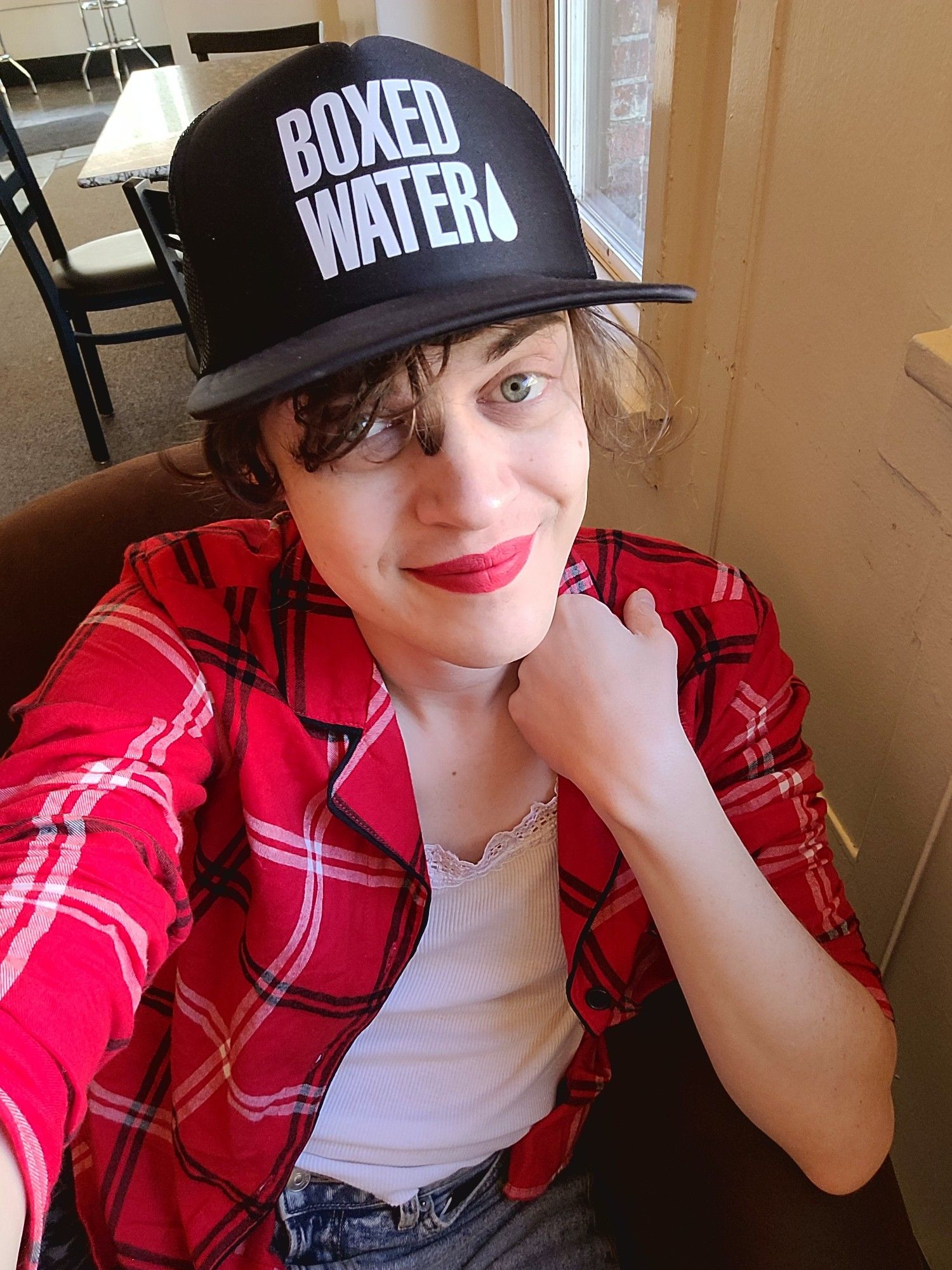 A girl in a black baseball cap, red flannel shirt, white tank top, and jeans