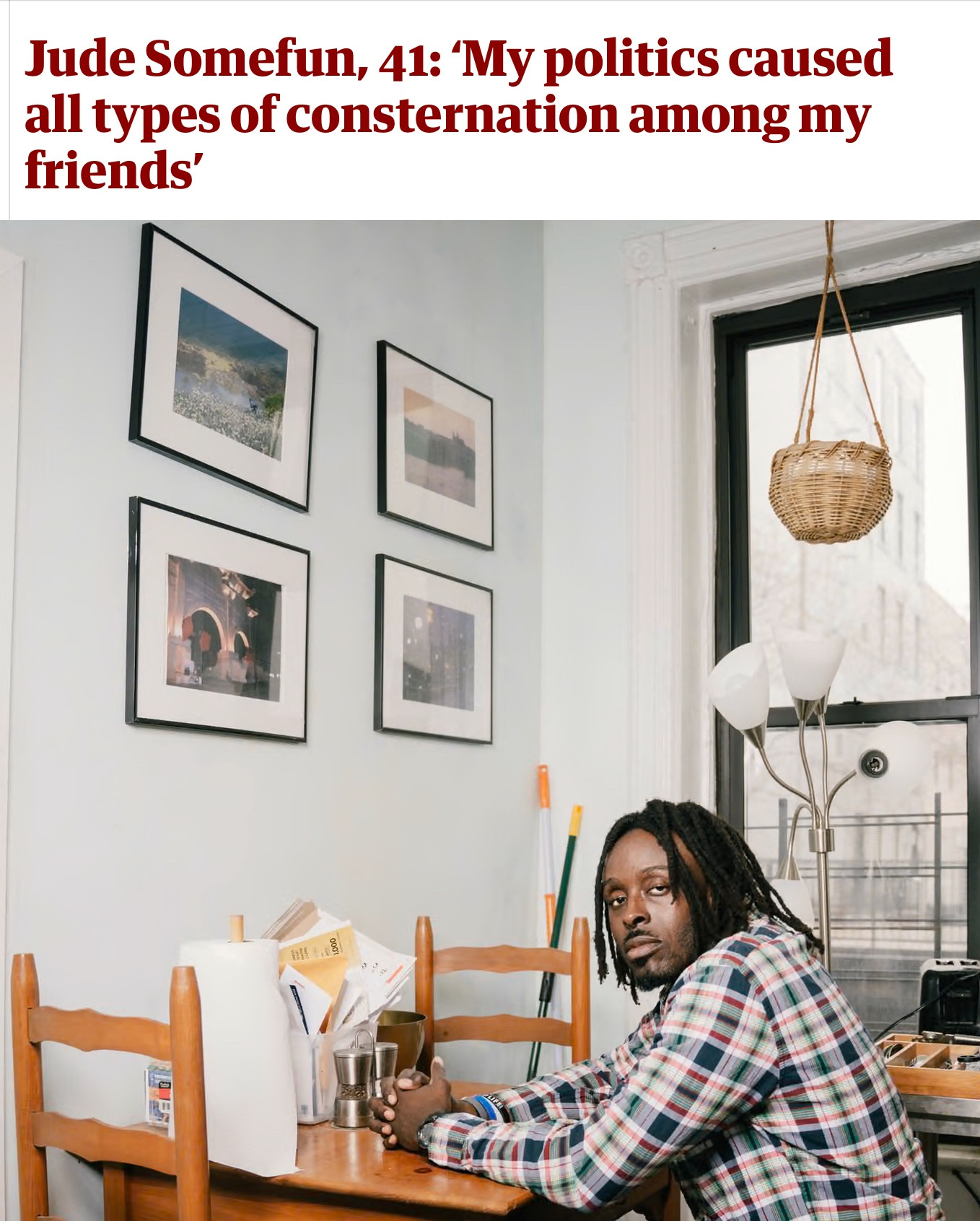 Heading: Jude Somefun, 41: ‘My politics caused all types of consternation among my friends’

Photo of a young Black man in a plaid shirt with locs sitting alone at his kitchen table. He is seated facing the wall with his fingers intertwined and his hands resting on the table while his head is turned so that he is looking at the camera over his left shoulder.