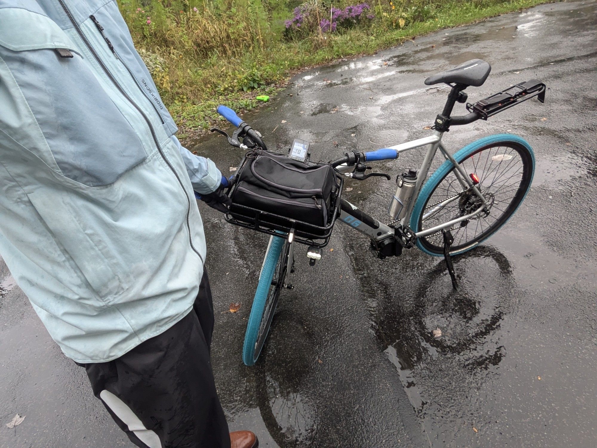 Man in rain jacket, rain pants, and waterproof boots leaning on an eBike in the rain.