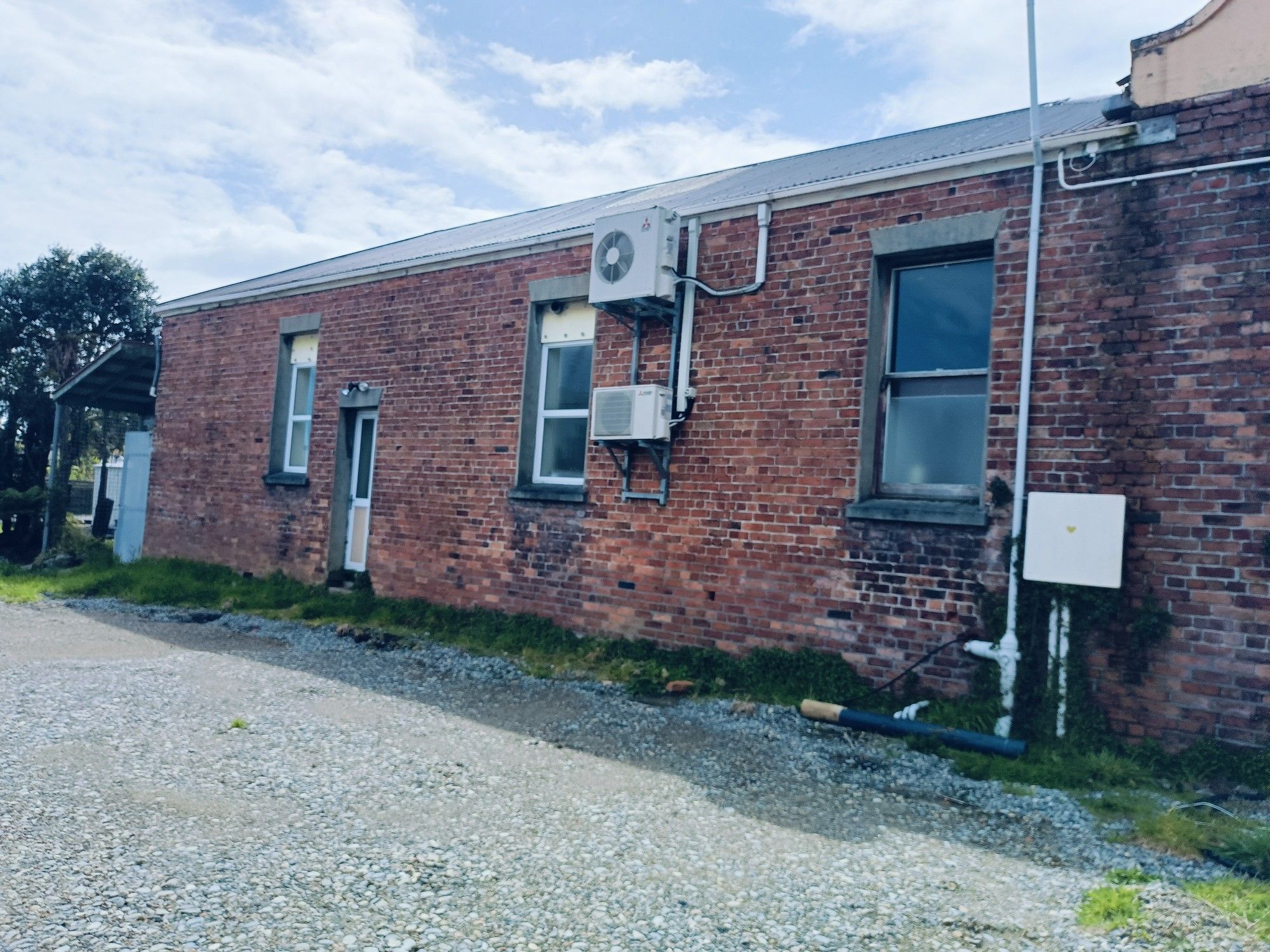 A wall of a non-descript red brick building with 3 small windows, a tiny door & heat pump attached to the outside. Absolutely no defining features.