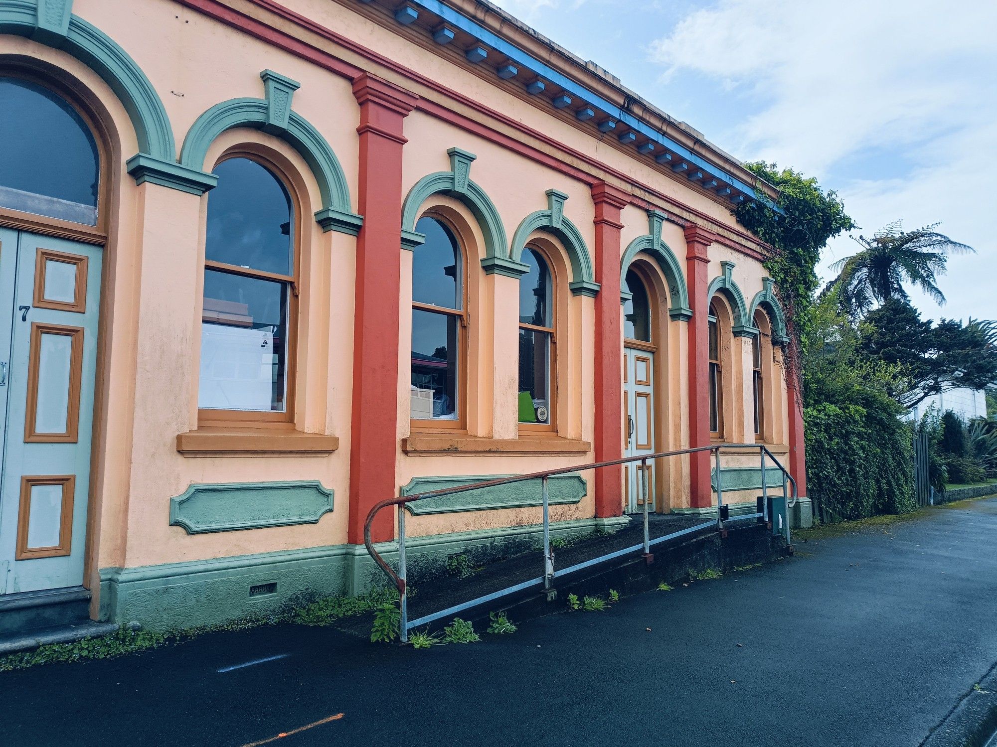 The front of an art deco building. There are several arched windows occupying most of the front face, plus an ornate arched door pained blue. The building is peach coloured with blue, orange & red trim.