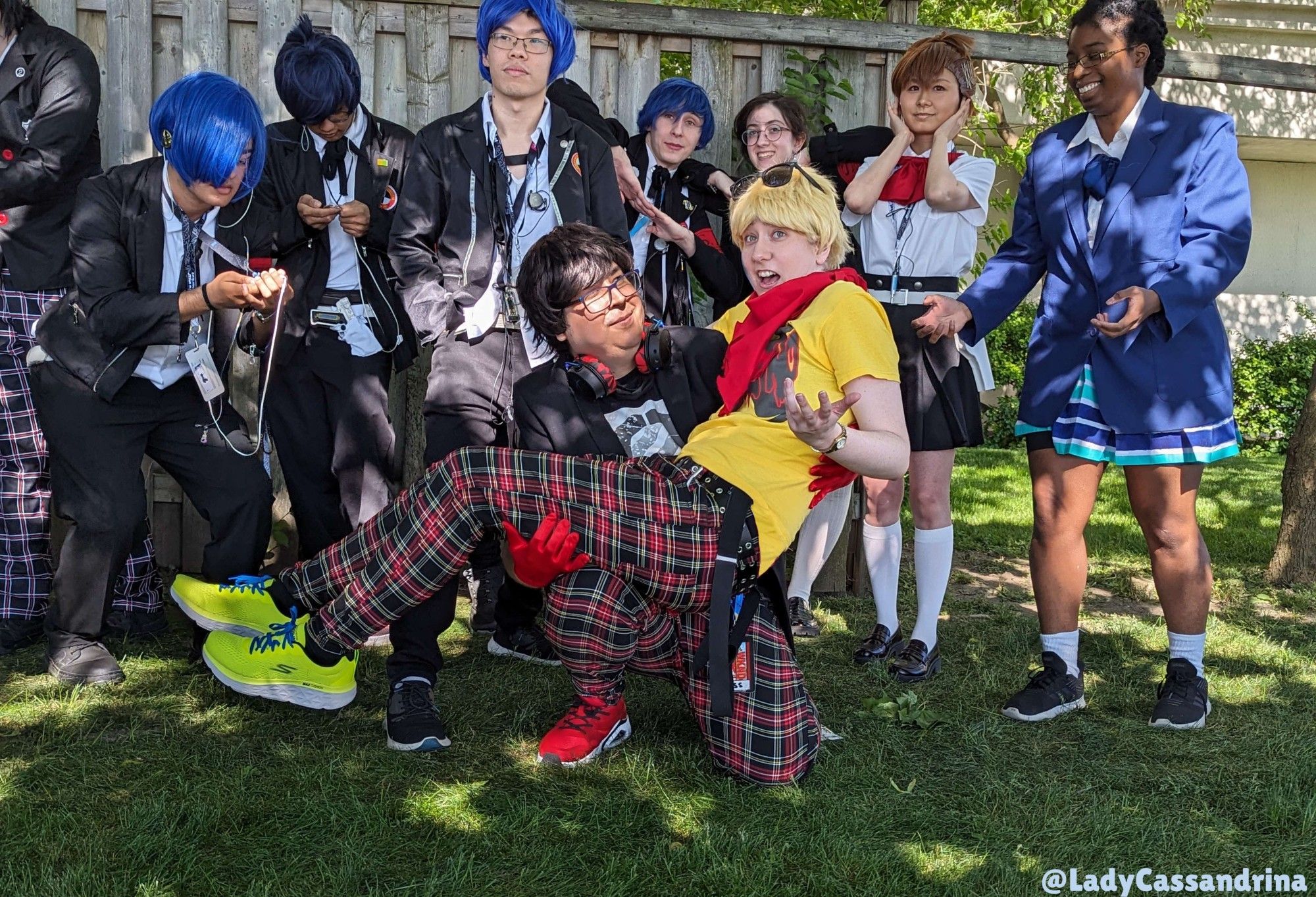 Anime  North Persona Photoshoot. Antho (as Dancing Joker) holds me (Dancing Ryuji) princess style. We're surrounded by P3 and Shin Megami cosplayers. A Makoto and Kotone smile brightly in the back while posing.