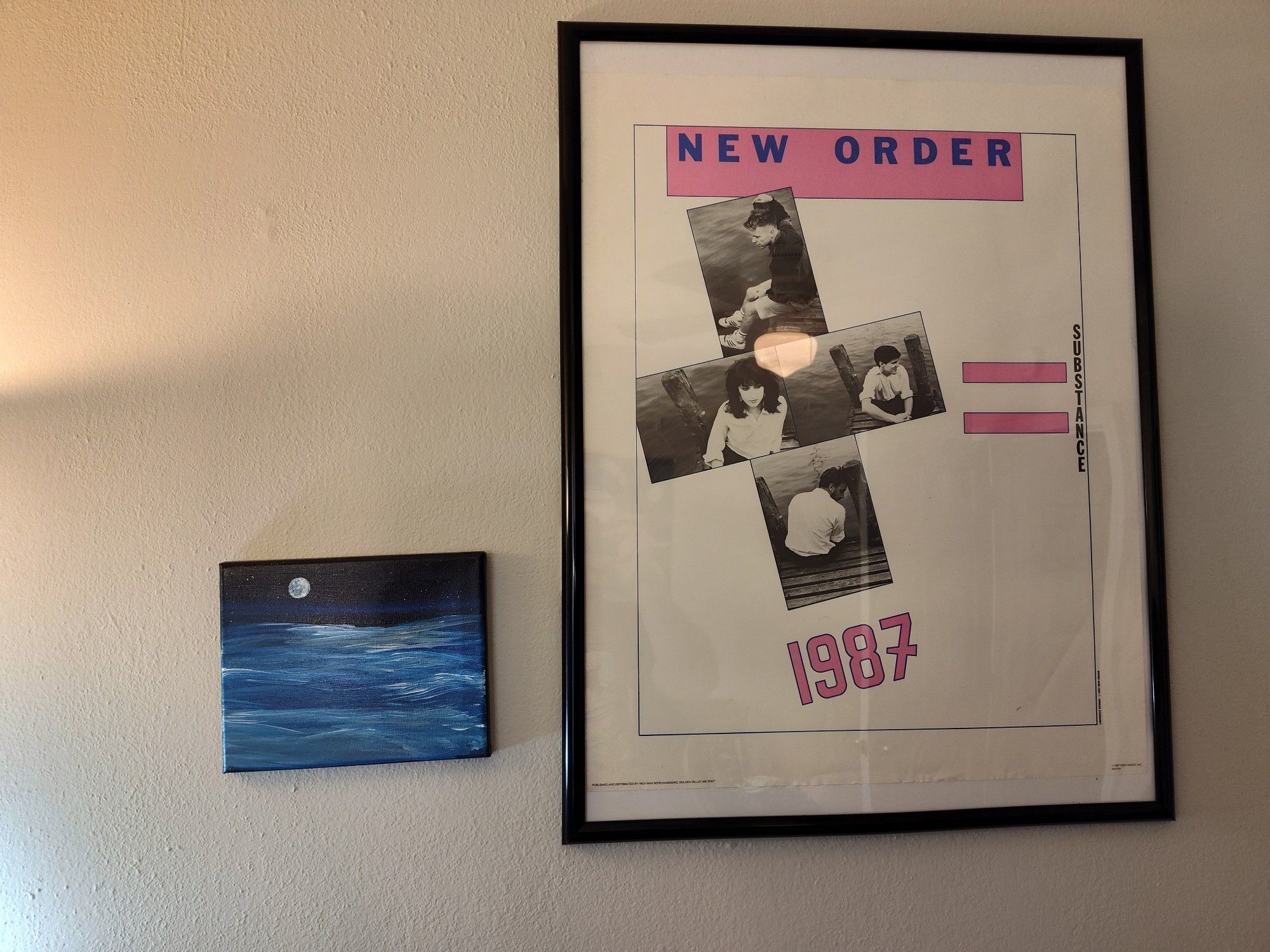 A photo of a wall of my music studio, featuring a vintage poster for the band New Order and a painting of a body of water at night