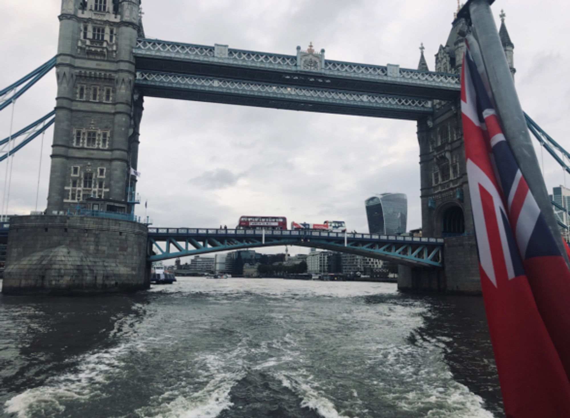 Shot from the river beneath Tower bridge, bridge in background with red bs going over it and water wake in foreground