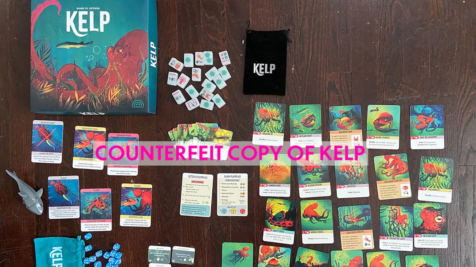 Box and components from a counterfeit copy of the Kelp board game, originally posted to publisher Wonderbow Games' website. Big pink text in the middle reads: "counterfeit copy of Kelp"