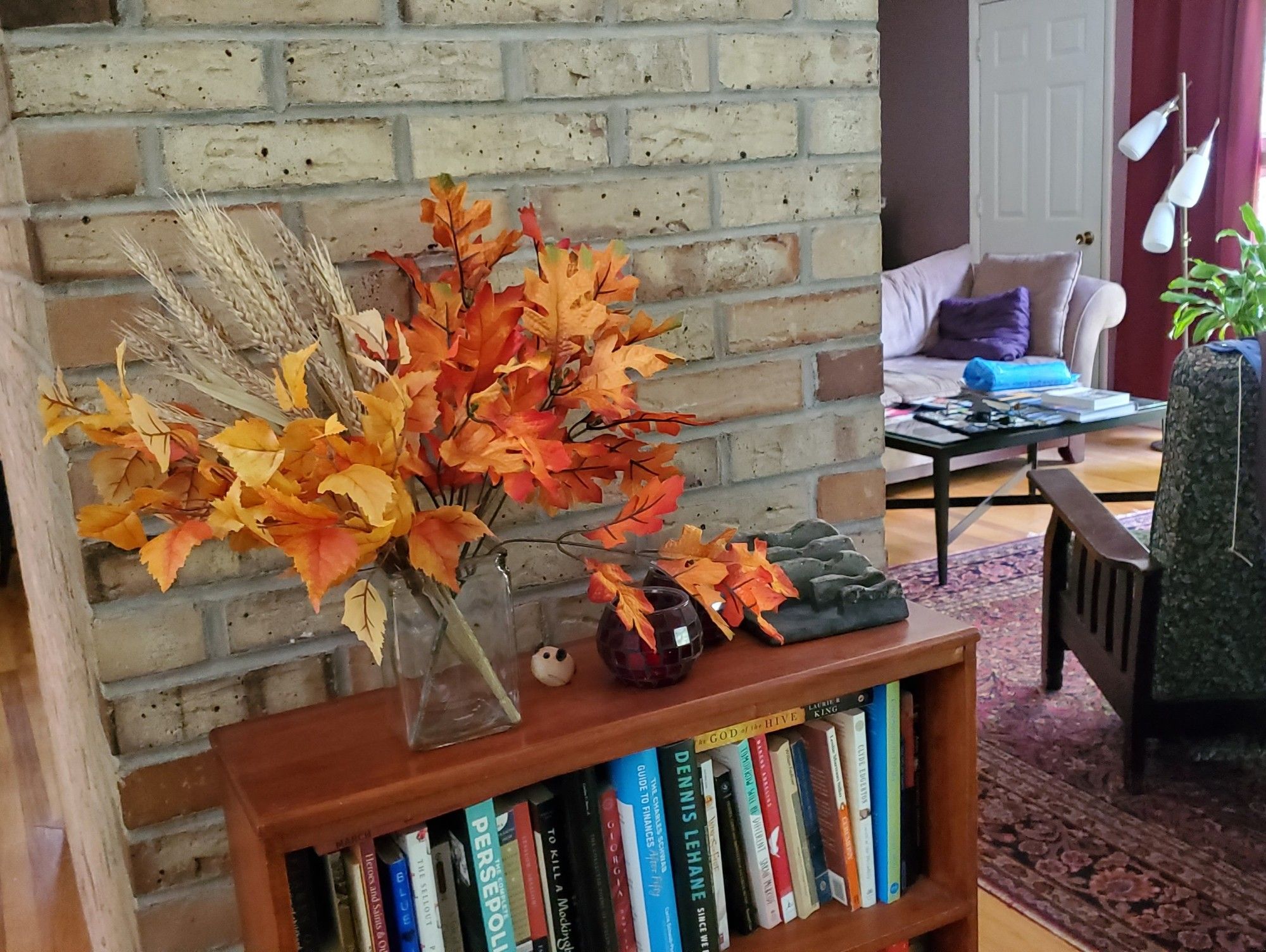 Photo of fall leaf arrangement on bookcase against brick fireplace inside home