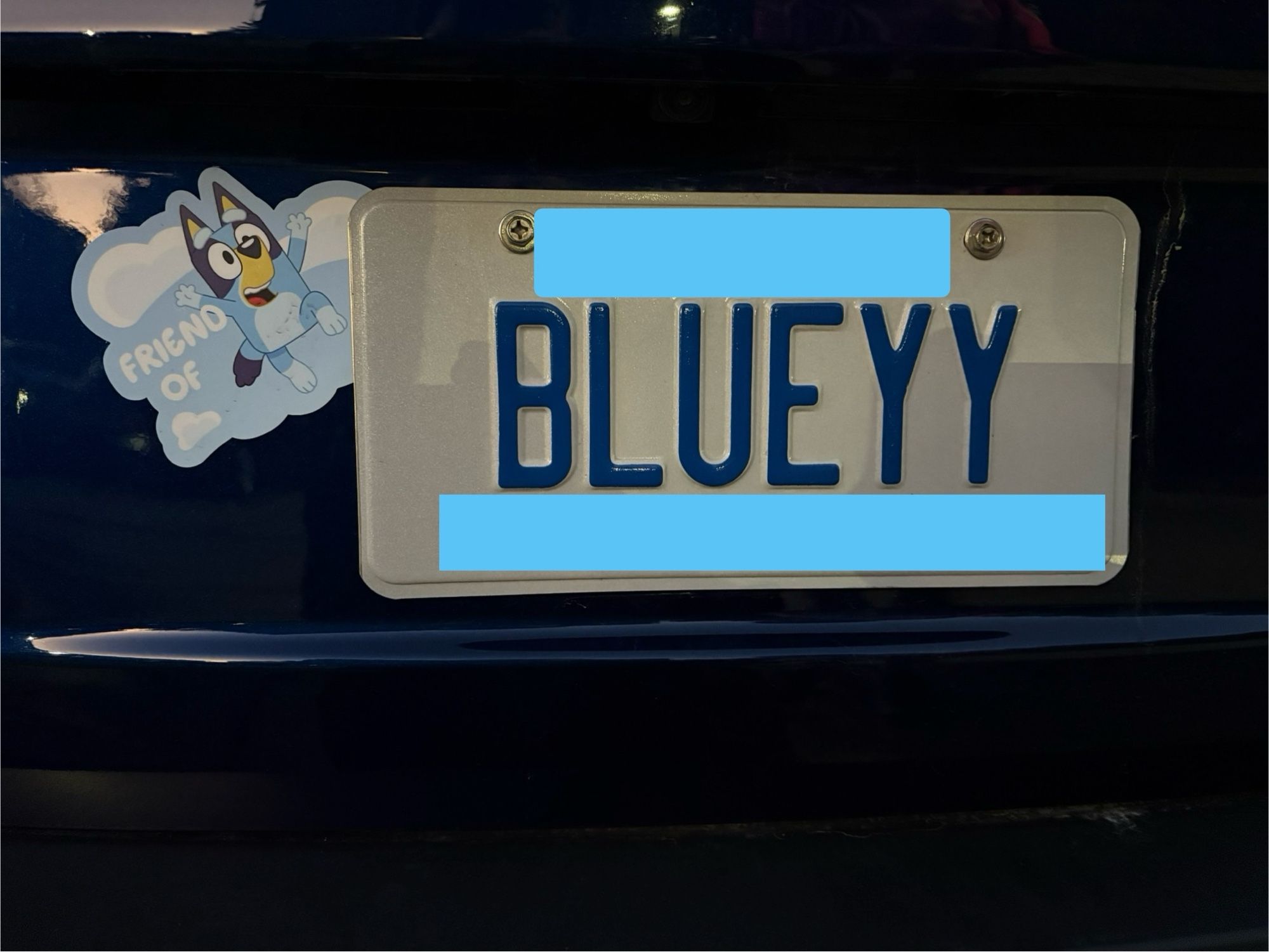 Blue car with Bluey license plate- to the top-left of the license plate is a sticker with Bluey with the text “Friend of”