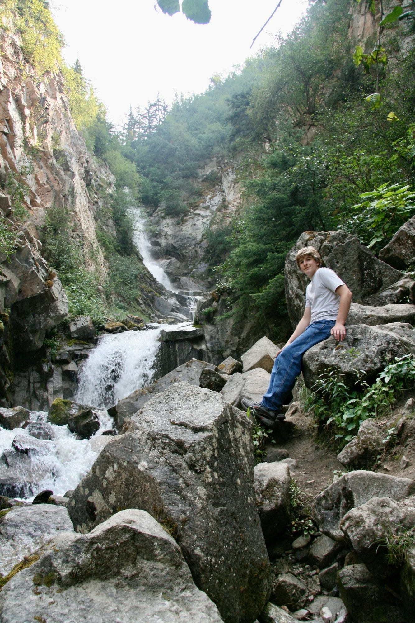 My son Steven, age 15, perched on a boulder beside a waterfall in rugged green Alaska.