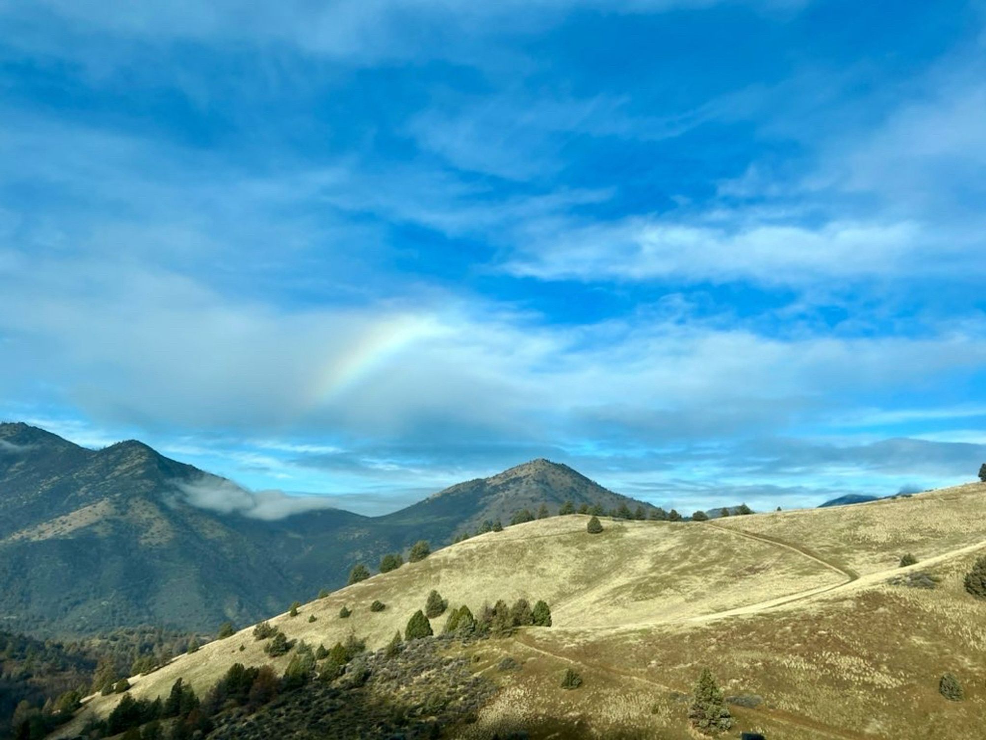 A smudge of rainbow in the clouds, over the hills and mountains in Siskiyou county, California.