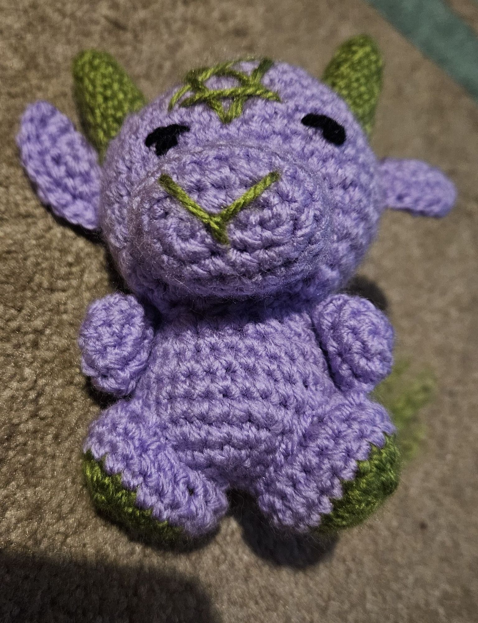 Crocheted lilac and green toy with horns and tail. Imagine a cute lilac baby baphomet!