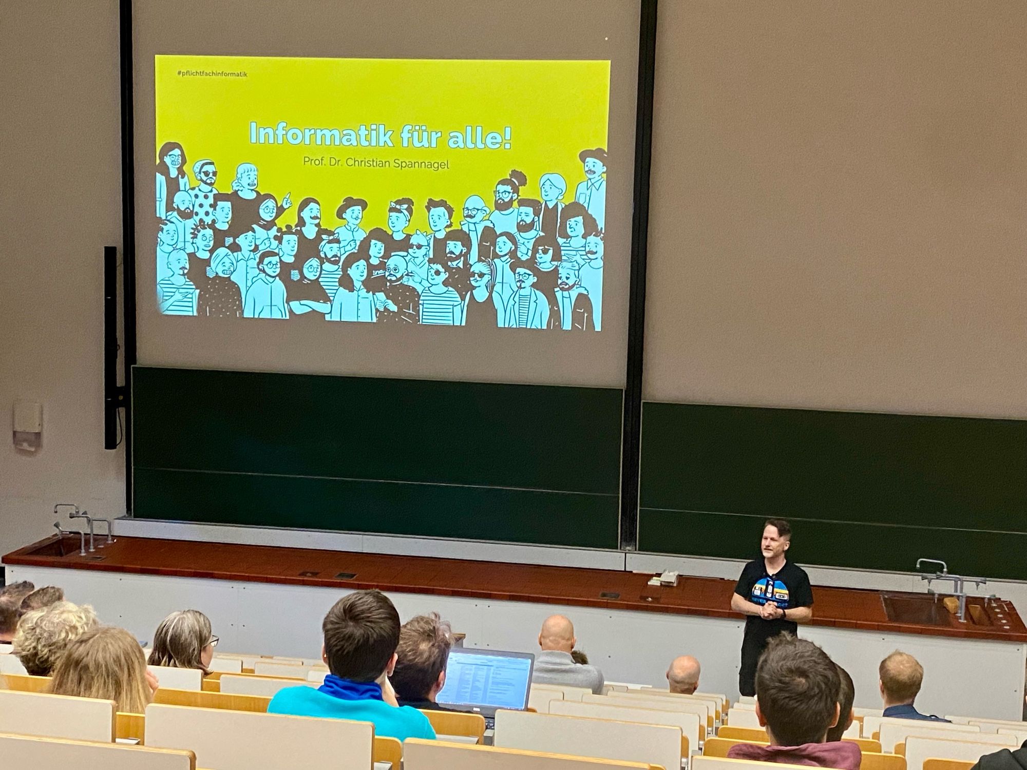 Prof. Dr. Christian Spannagel, PH Heidelberg, bei seiner Keynote im Hörsaal. Hinter ihm die Startfolie mit Titel „Informatik für alle“