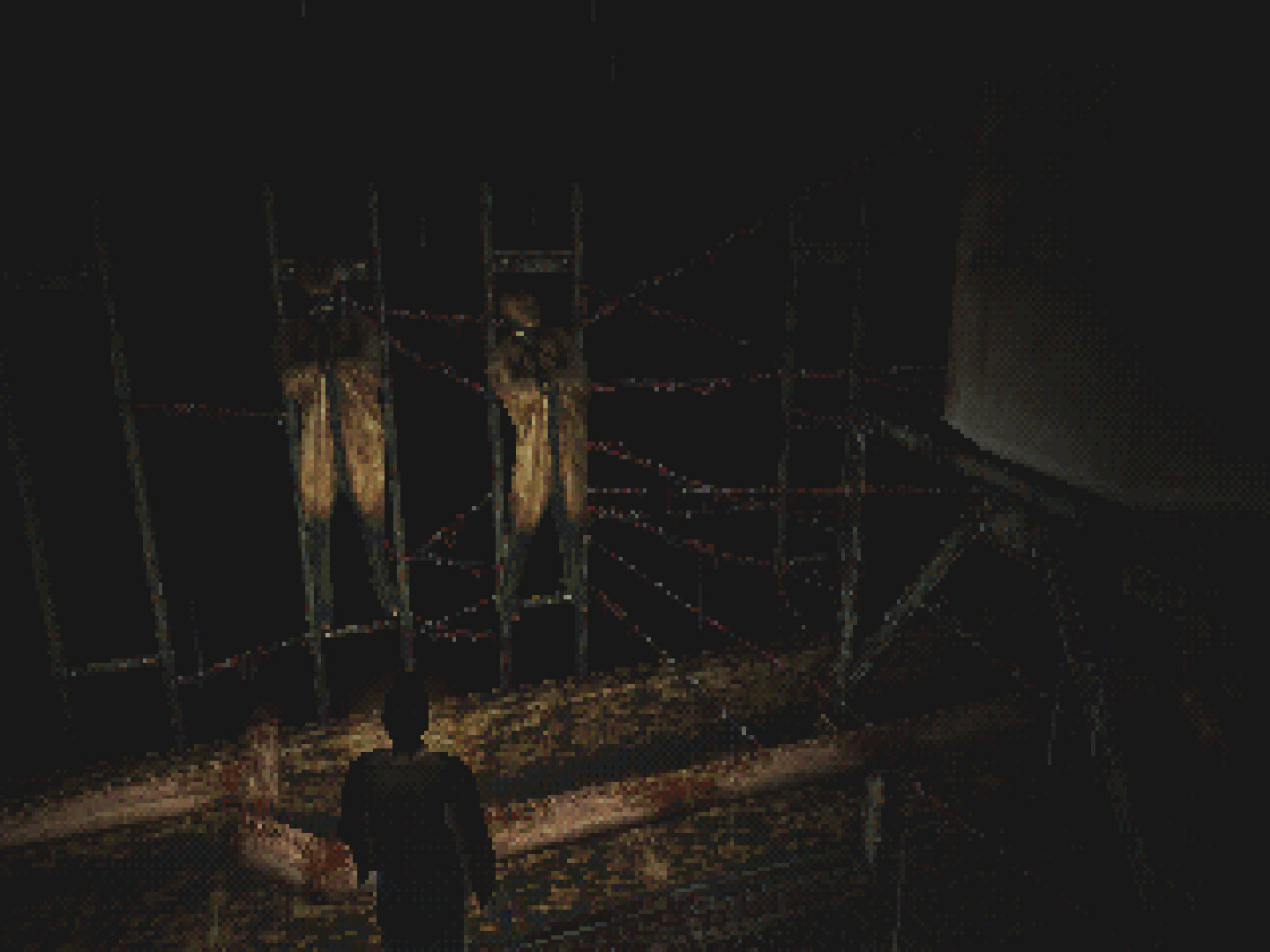 A screenshot from Silent Hill. Two corpse-like shapes are strung up on a web of barbed wire.