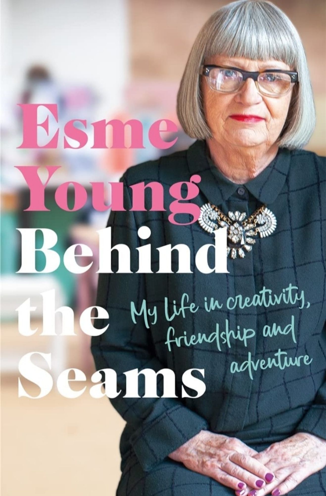 Book cover of Esme Young's "Behind the Seams | My life in creativity, friendship and adventure" (which features the fabulous Esme Young in red lipstick and purple nail polish and with a very cool necklace)