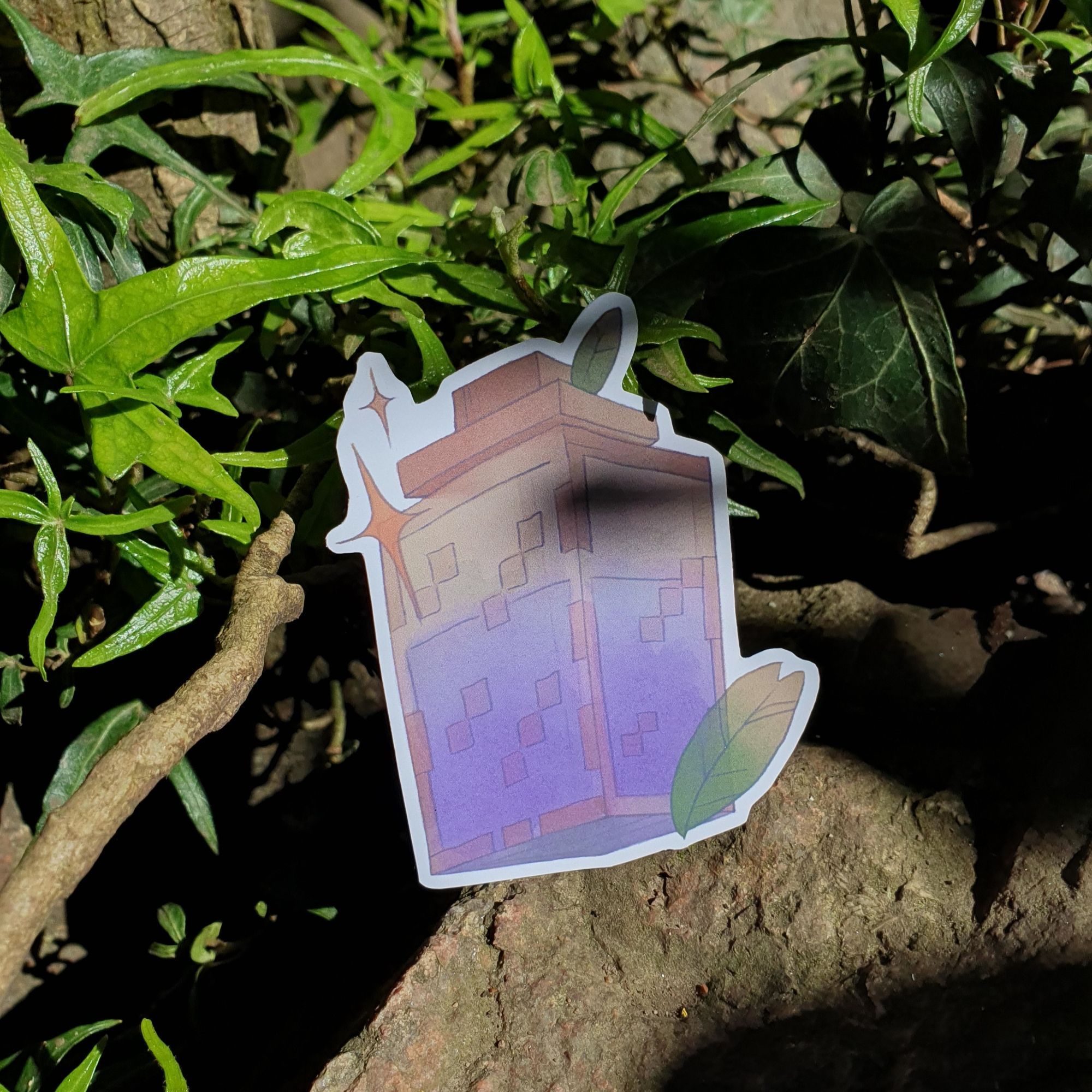 square photograph of a cut out sticker outside, placed on a large rock with leaves and greenery behind it. the sticker design is of a cubic jar filled with purple liquid, and is in the style of the video game minecraft. in the background is a dappled sunlight natural environment.