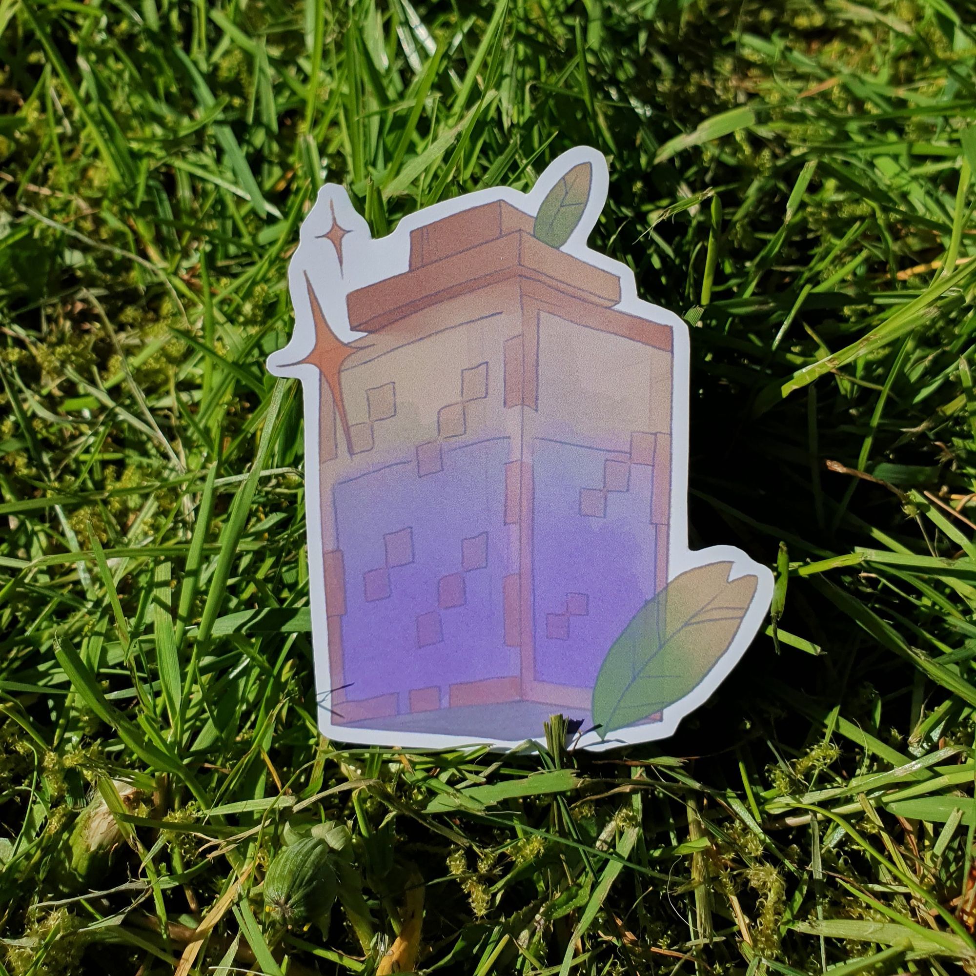 square photograph of a cut out sticker outside, placed on grass in sunshine. the sticker design is of a cubic jar filled with purple liquid, and is in the style of the video game minecraft.