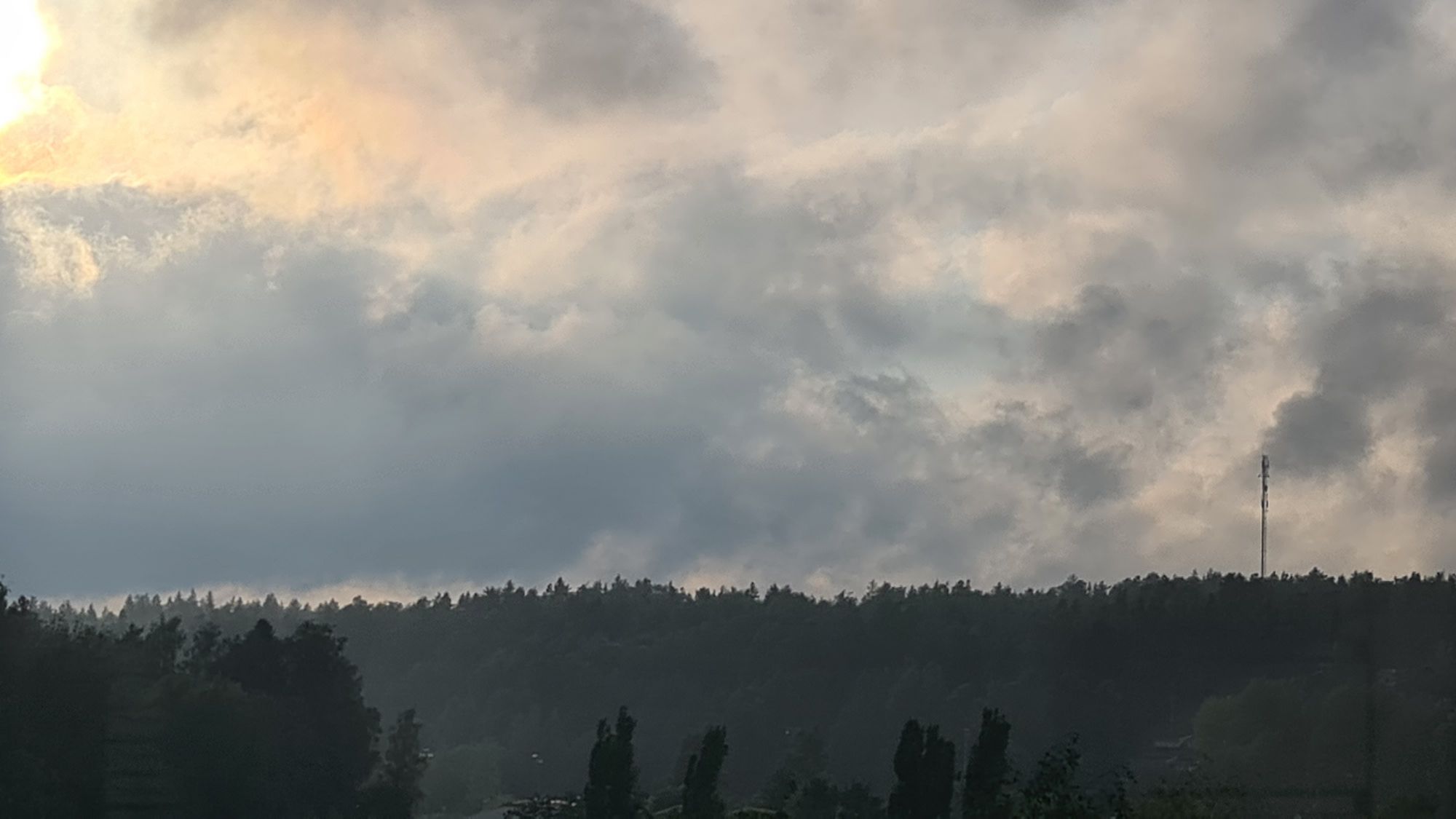 Rainy evening sky with golden sunlight breaking through the clouds. Moist air is making the forest further away look hazy.