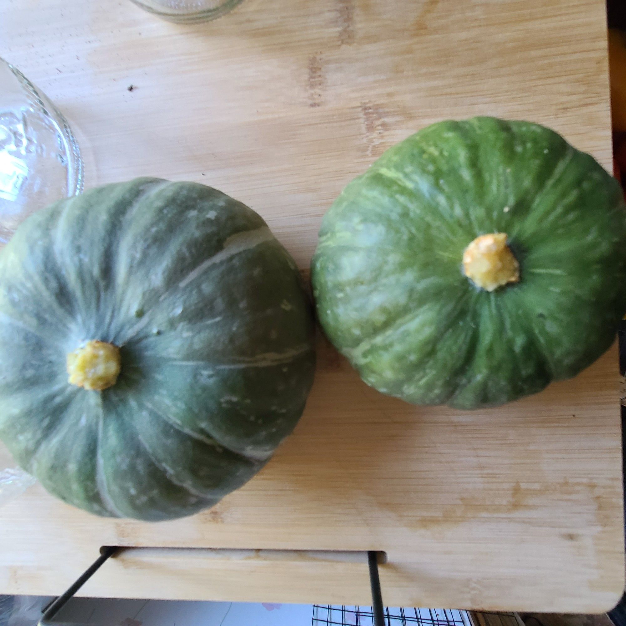 2 small round squat gren slightly varigated squash with small yellow stems on wooden surface