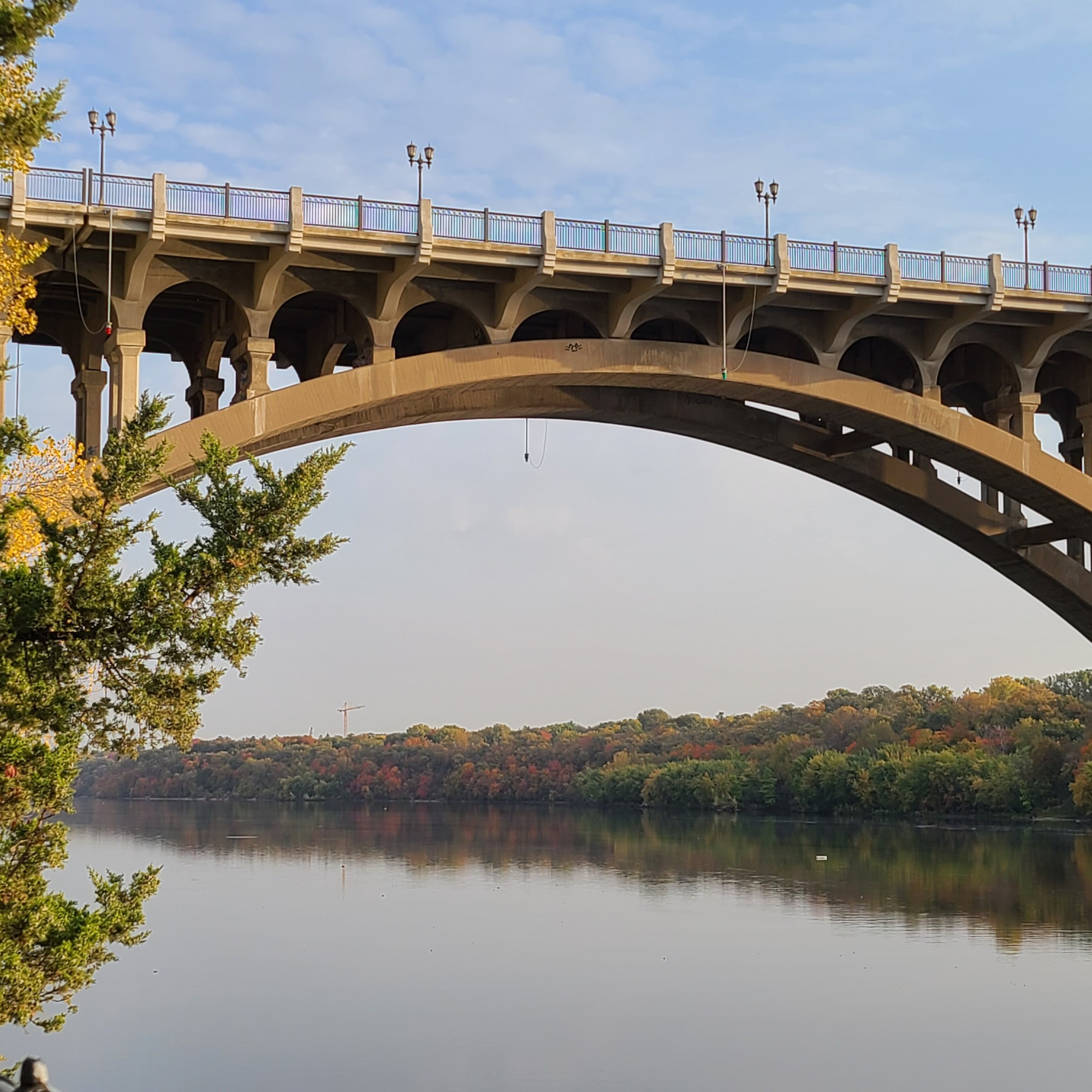 Ford Bridge arching over still Mississippi River, reflecting below, just changing trees on the banks either side