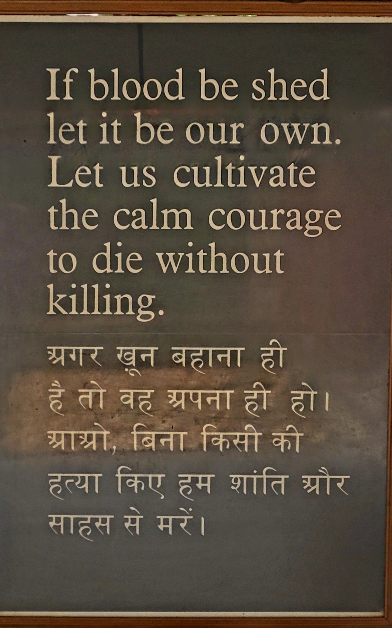 Brown poster with white text in English and then Hindi. English text reads:

If blood be shed
let it be our own.
Let us cultivate
the calm courage
to die without
killing.