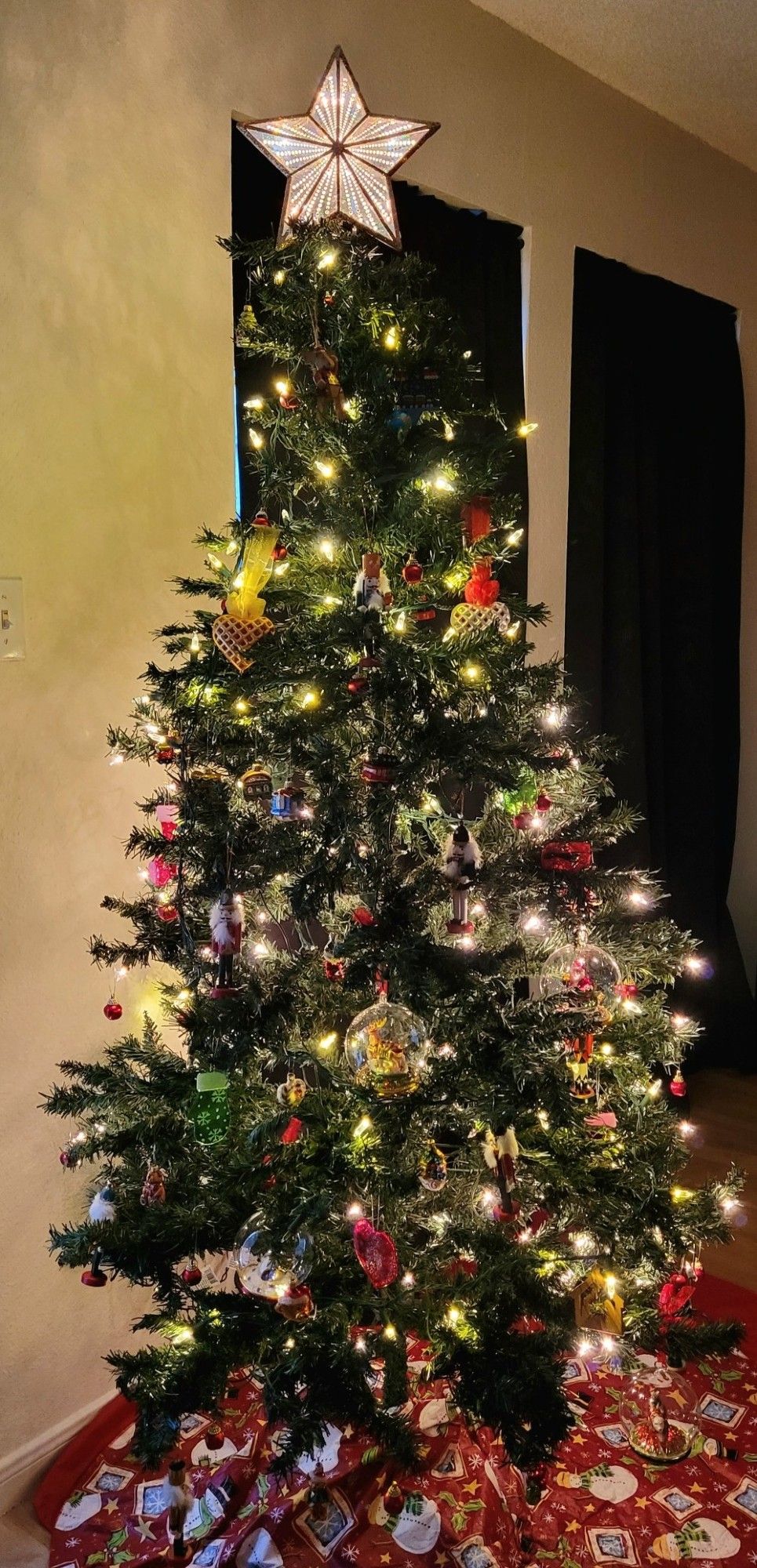 A lighted Xmas tree with a lighted star-shaped tree topper. Red tree skirt.