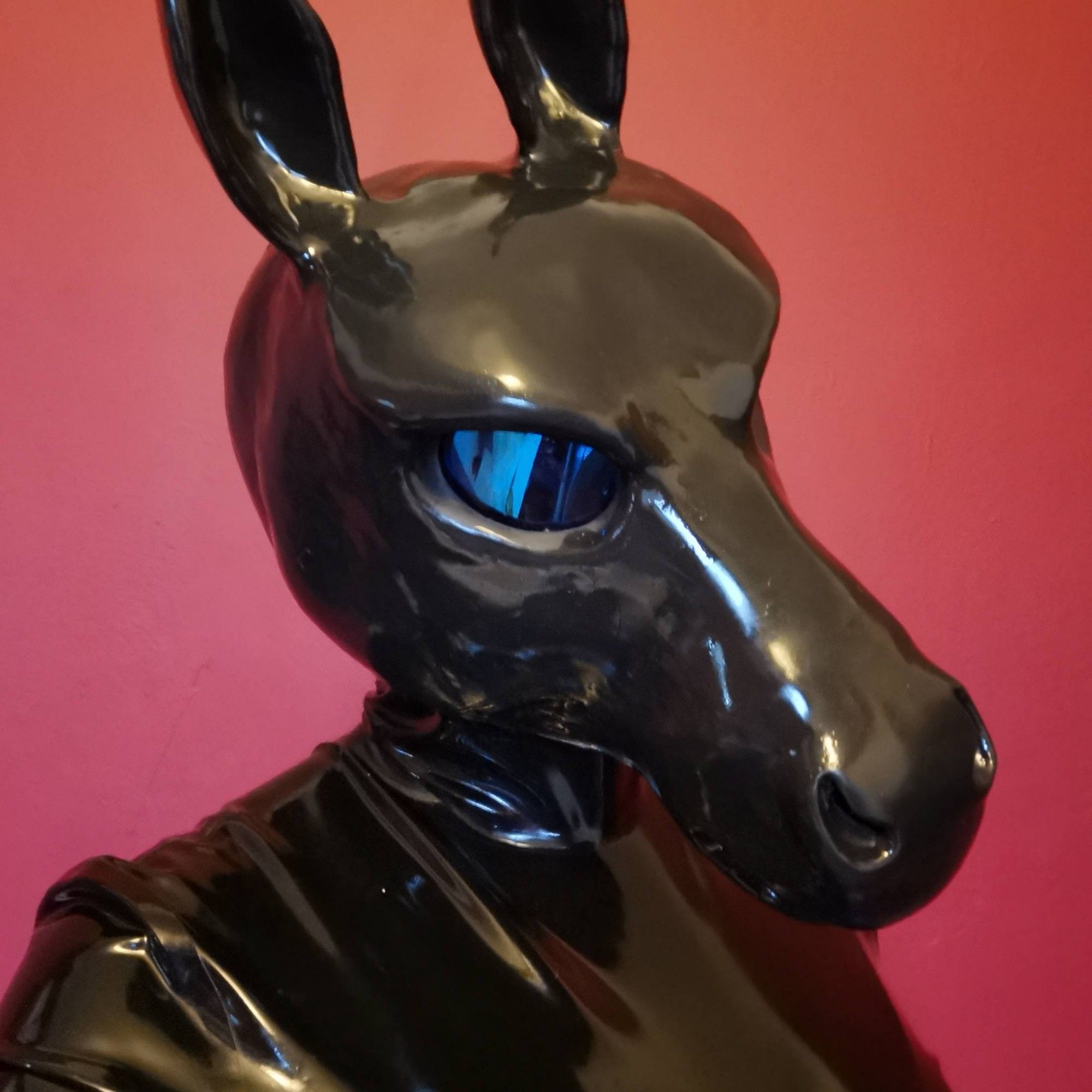 A horse head shaped gas mask on a figure wearing a black latex catsuit